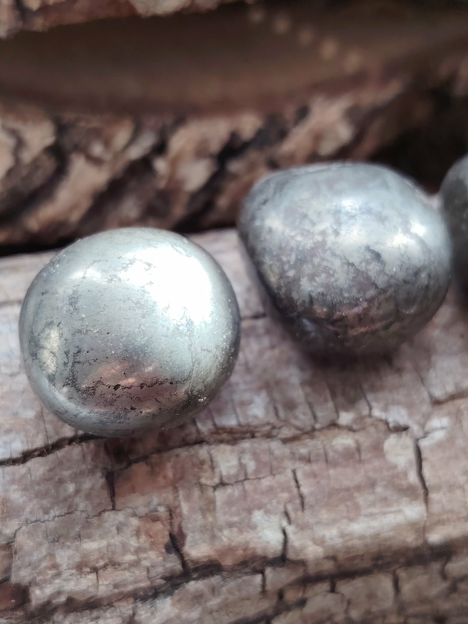 Deux pierres roulées de pyrite aux reflets métalliques dorés posées sur du bois craquelé, éclats lumineux, pour inviter à la protection, la confiance en soi et la clarté mentale.