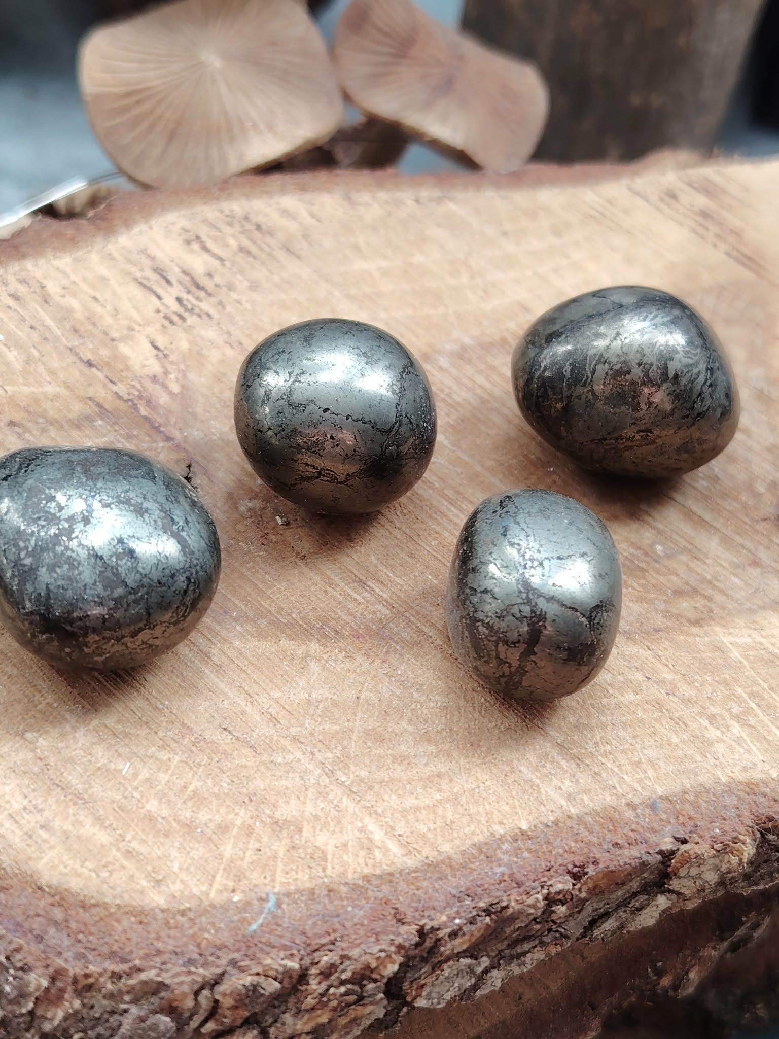 Quatre pierres roulées de pyrite aux reflets métalliques dorés posées sur une tranche de bois, pour soutenir confiance, protection et clarté.