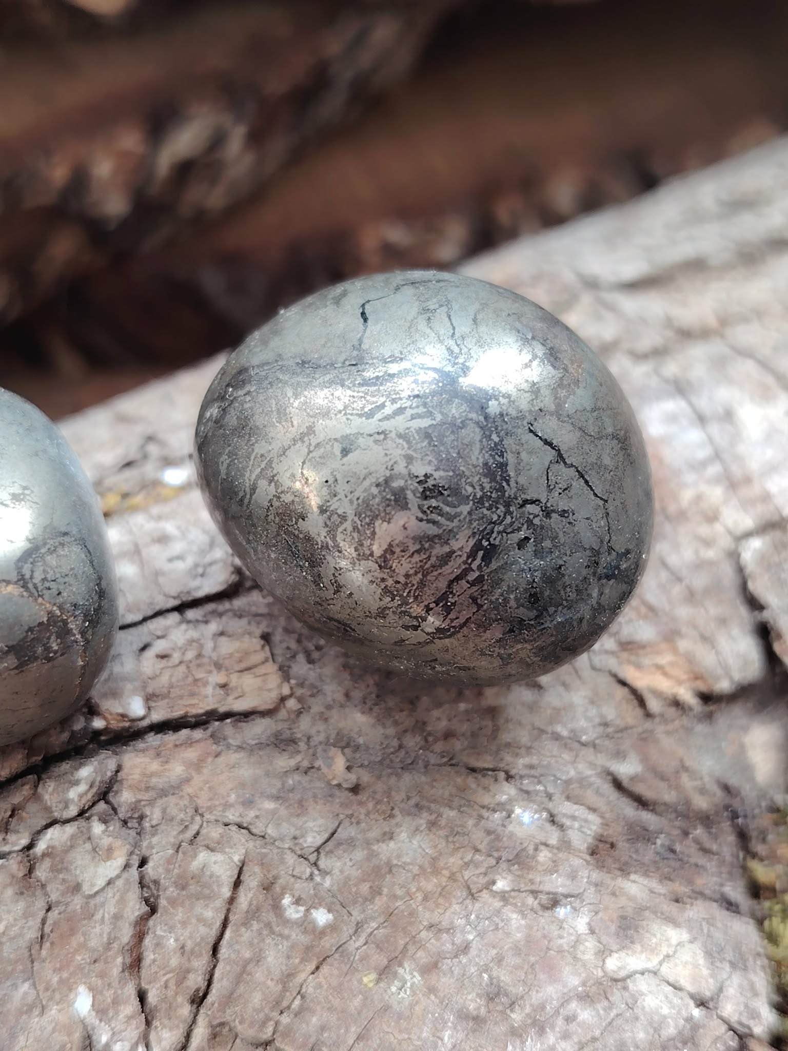 Pierre roulée de pyrite aux reflets métalliques dorés posée sur du bois craquelé, éclat lumineux naturel, pour inviter à la protection, la confiance et la clarté mentale