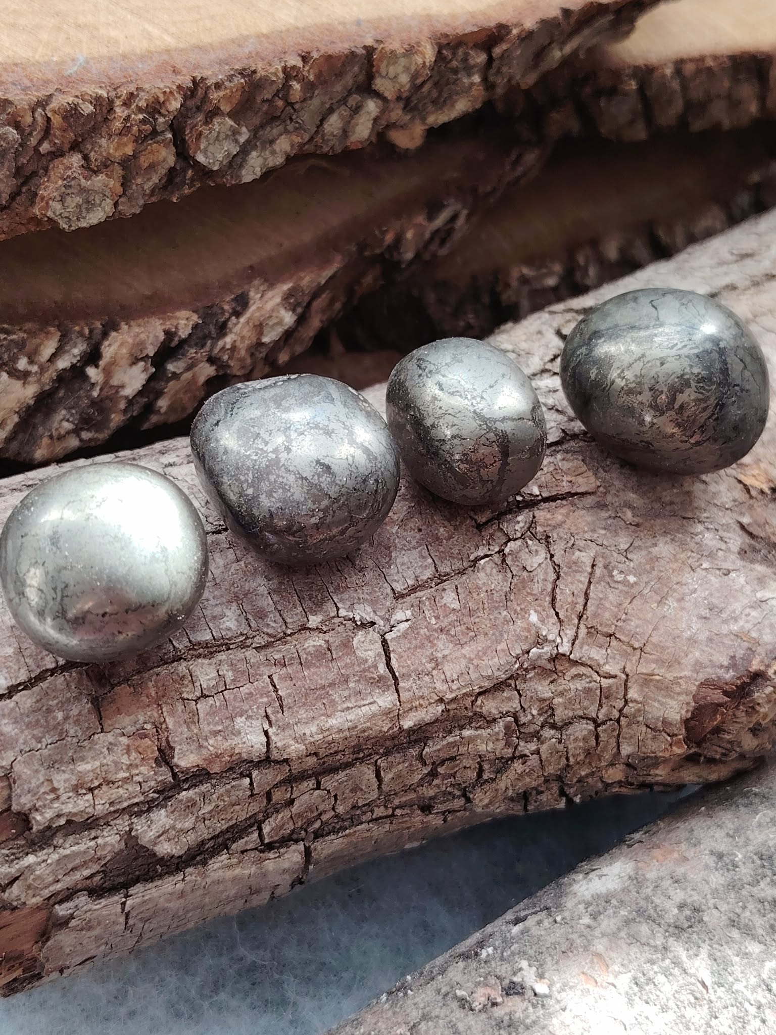 Quatre pierres roulées de pyrite aux reflets métalliques dorés posées sur du bois naturel, éclats lumineux, pour inviter à la protection, la confiance en soi et la clarté mentale.