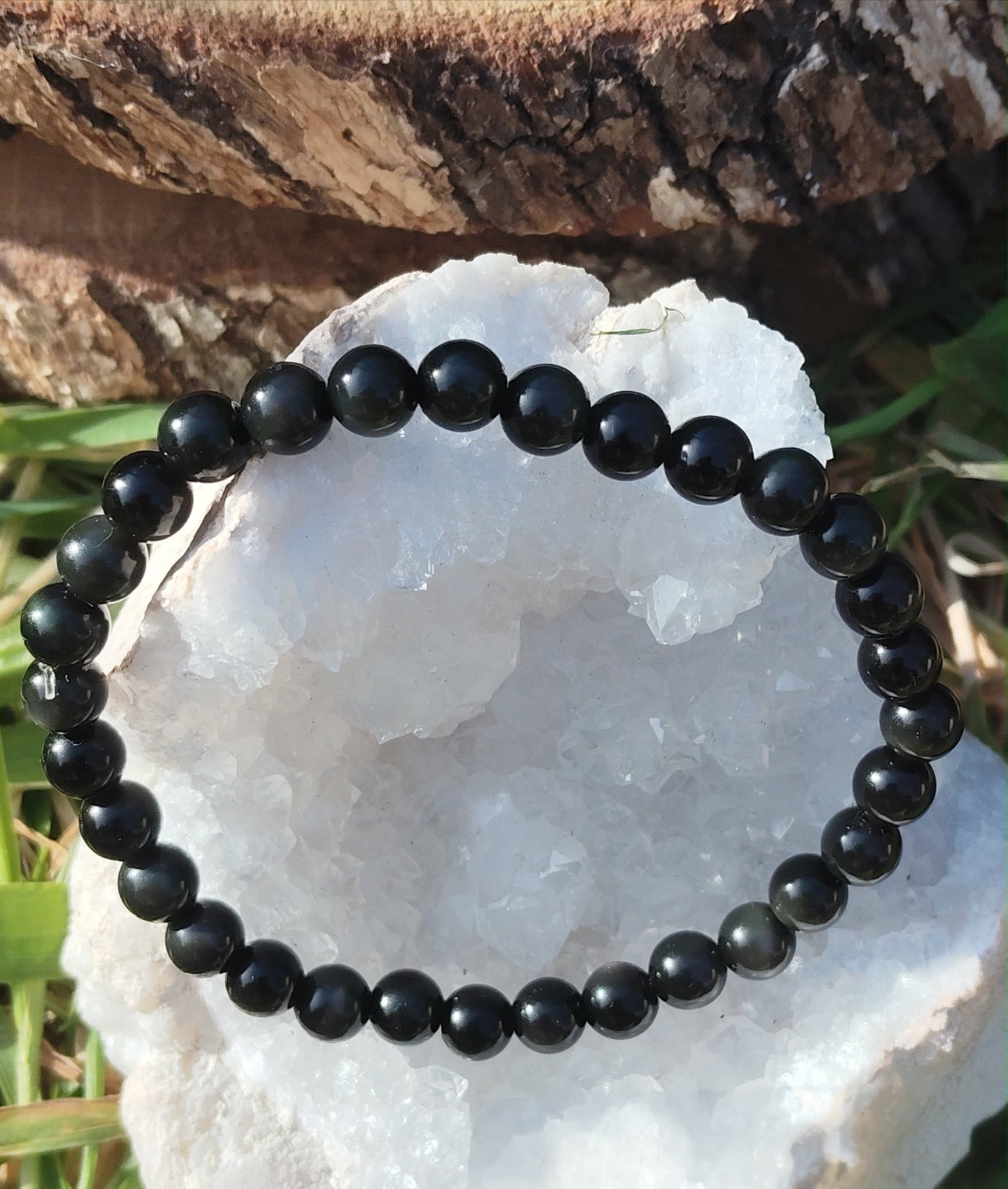 Bracelet obsidienne œil céleste 6 mm posé sur un amas de quartz blanc avec touches végétales, lucidité, recentrage et apaisement profond