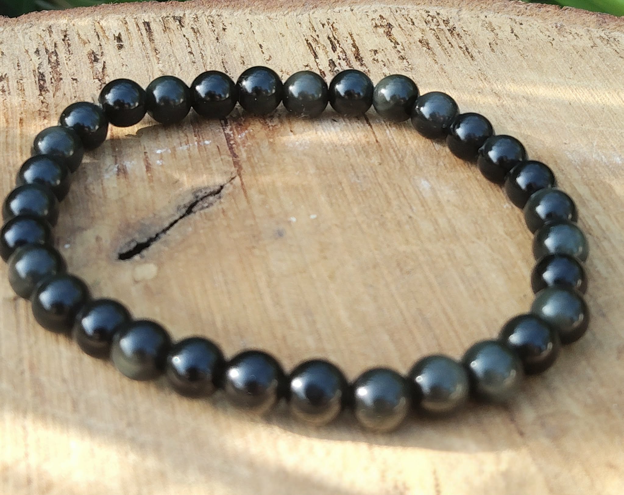 Bracelet obsidienne œil céleste 6 mm en perles noires sur planche de bois clair avec petite brindille, solidité, discernement et clarté mentale