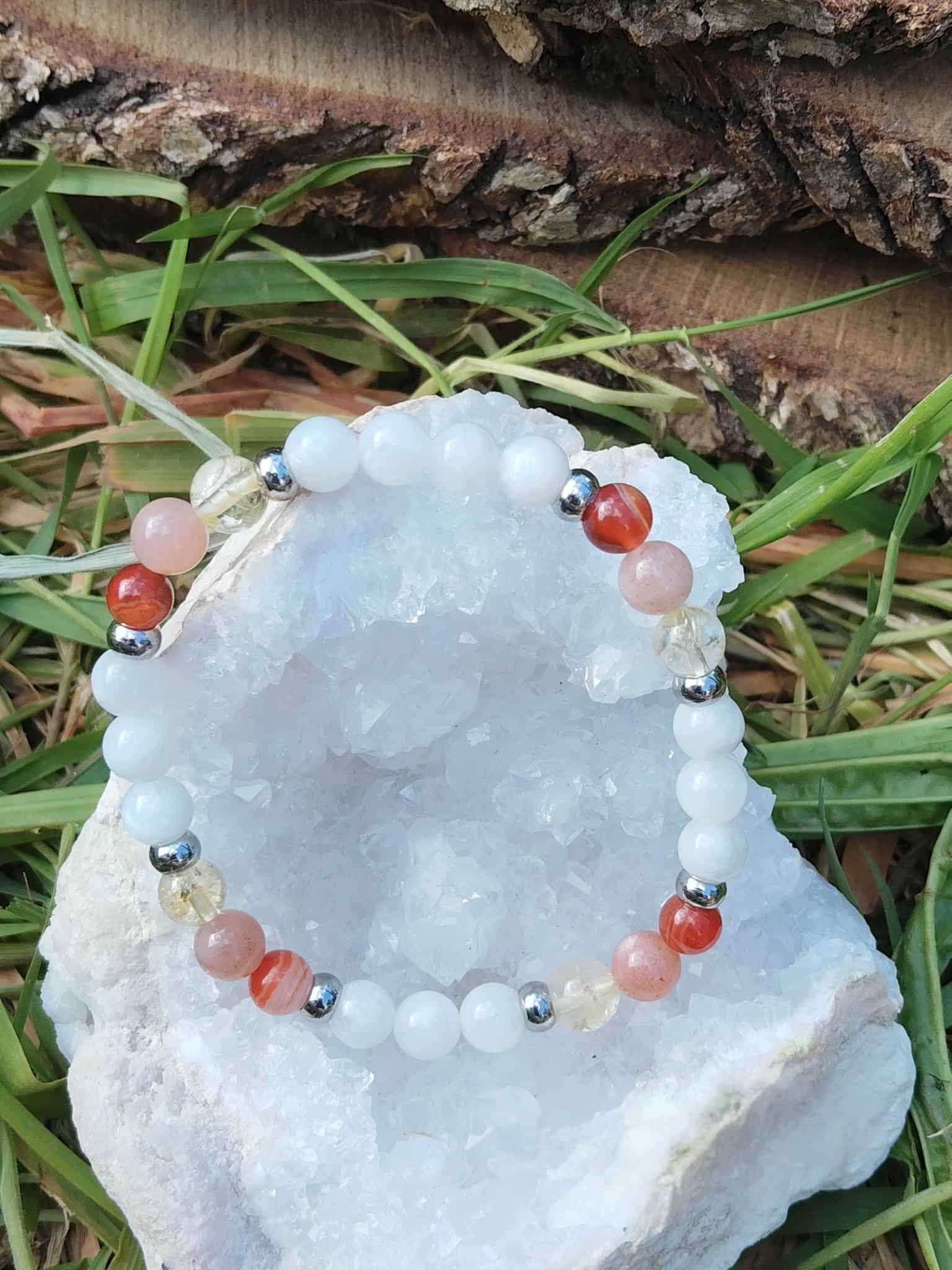 Bracelet PMA 6 mm posé sur pierre blanche parmi l’herbe, péristérite, pierre de soleil et cornaline pour vitalité sereine, douceur du cœur et confiance