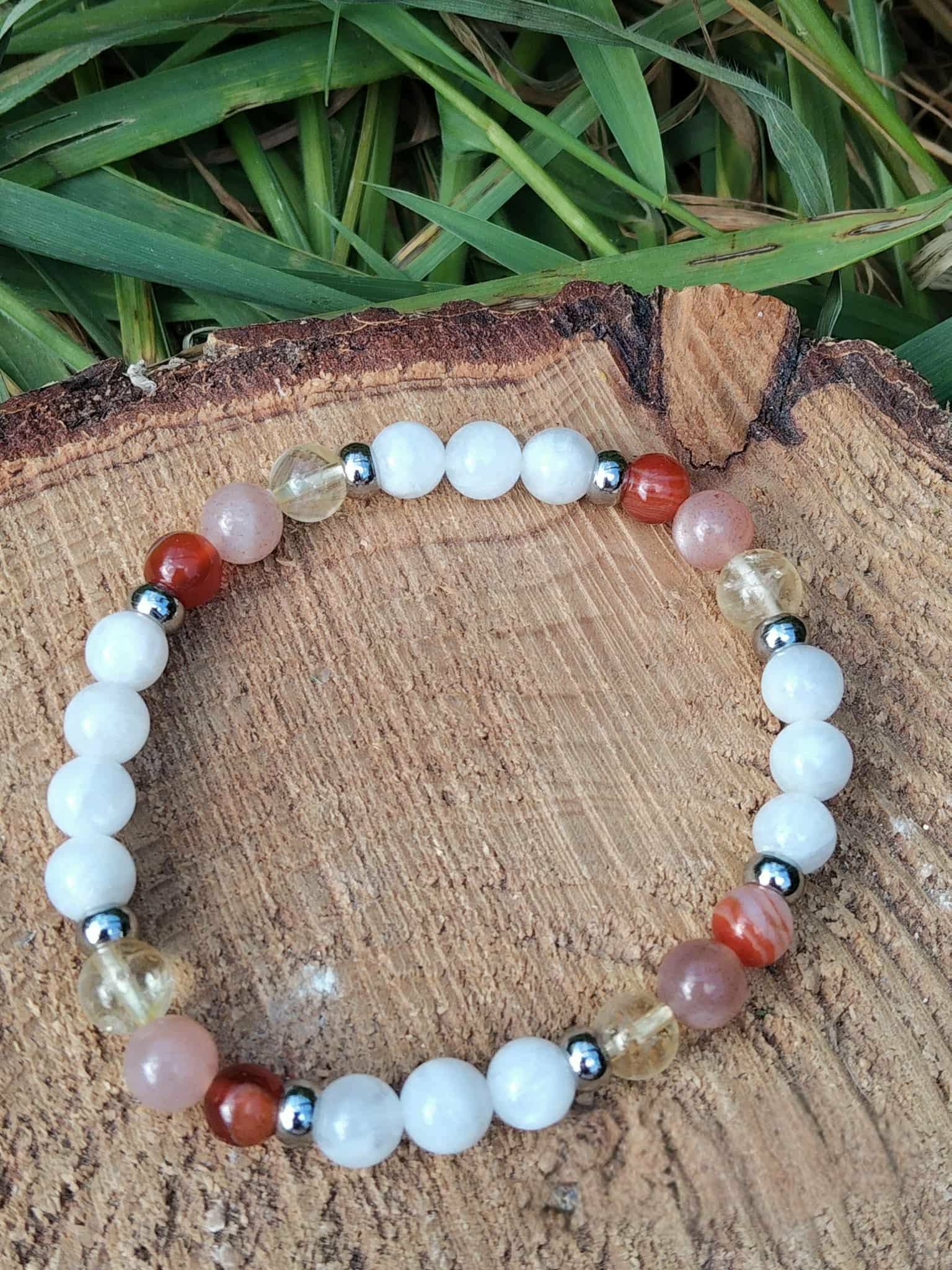 Bracelet PMA 6 mm posé sur rondin de bois avec feuillage vert, péristérite, pierre de soleil et cornaline pour courage doux, vitalité et stabilité émotionnelle
