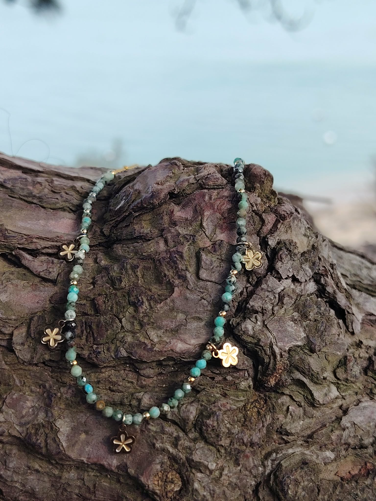 Collier doré vert africain facetté avec pendentifs fleur sur rocher en bord de mer, bijou acier inoxydable au style frais et lumineux