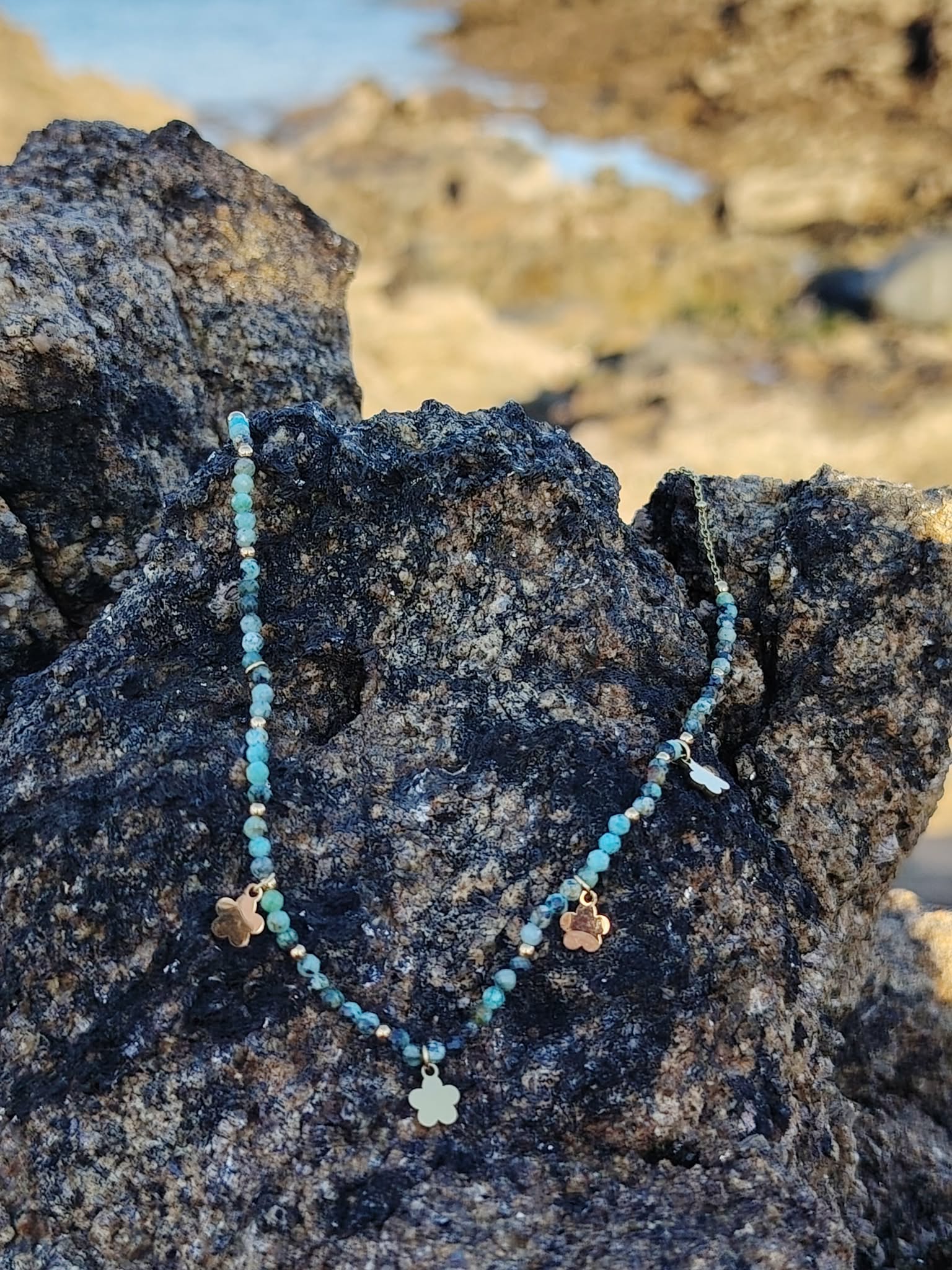 Collier doré vert africain facetté posé sur rocher en bord de mer en Bretagne, bijou féminin aux accents frais et équilibrés