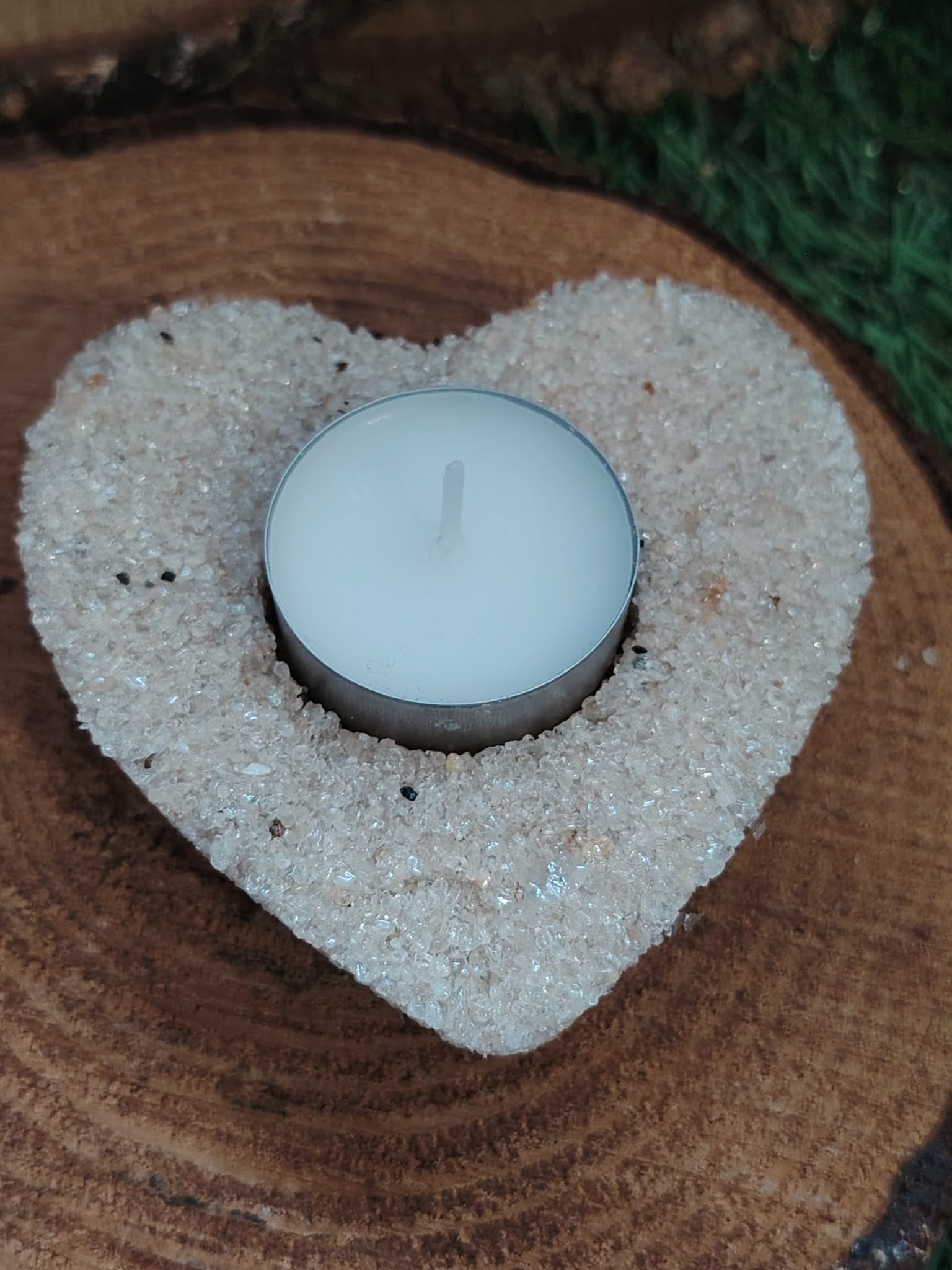 Bougeoir cœur en cristal de roche (quartz clair) posé sur rondin de bois, bougie chauffe-plat bleue au centre, décor naturel sombre, lumière douce, intention apaisement et clarté intérieure.