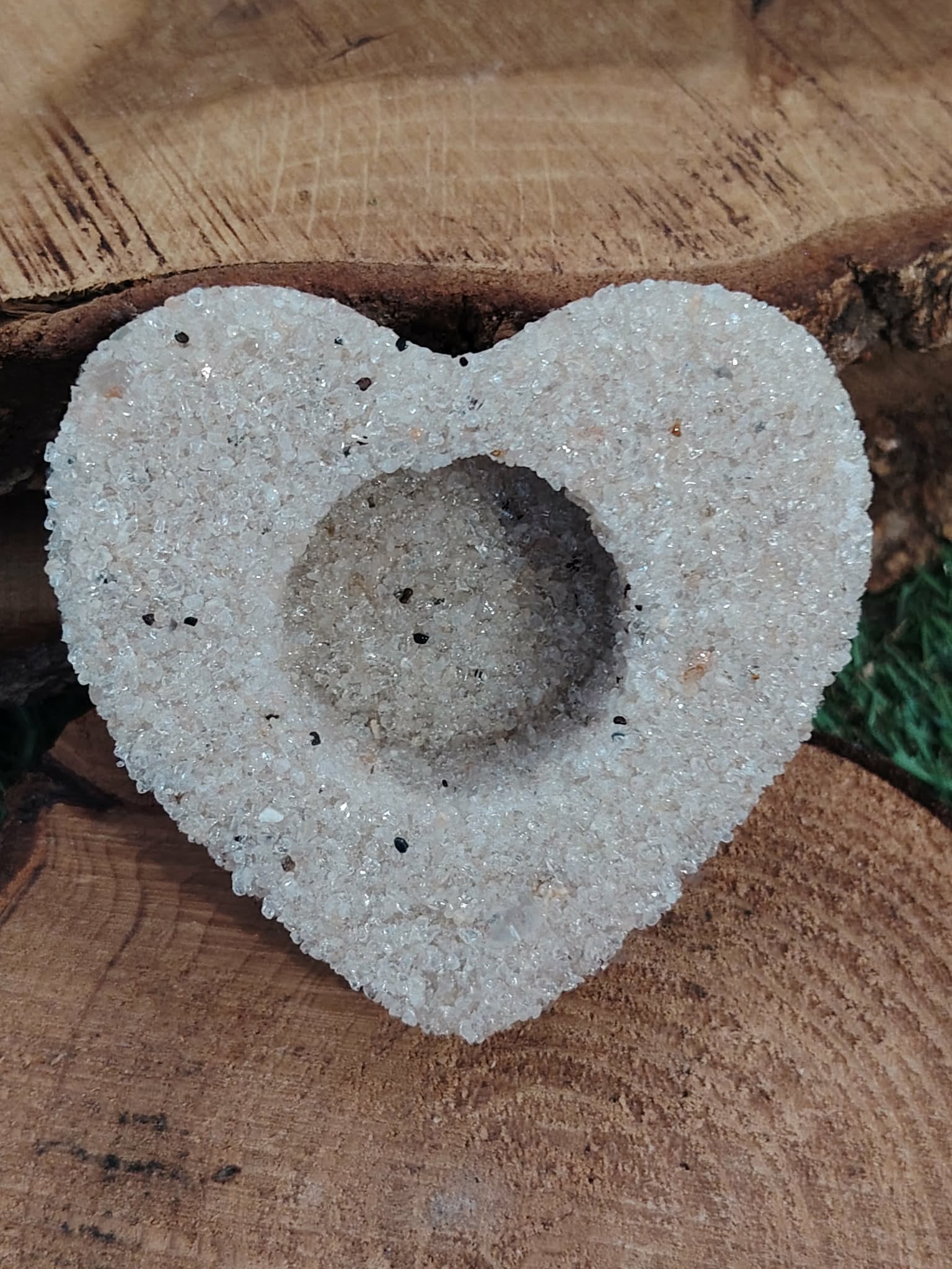 Bougeoir cœur en cristal de roche (quartz clair) posé sur rondin de bois, feuilles vertes en arrière-plan, cavité pour bougie chauffe-plat, déco naturelle, intention clarté et harmonie.