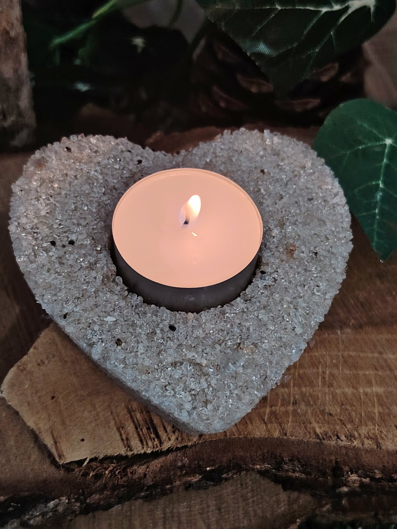 Bougeoir cœur en cristal de roche (quartz clair) avec bougie chauffe-plat allumée, posé sur rondin de bois et pierre sombre, ambiance douce, intention clarté et harmonie