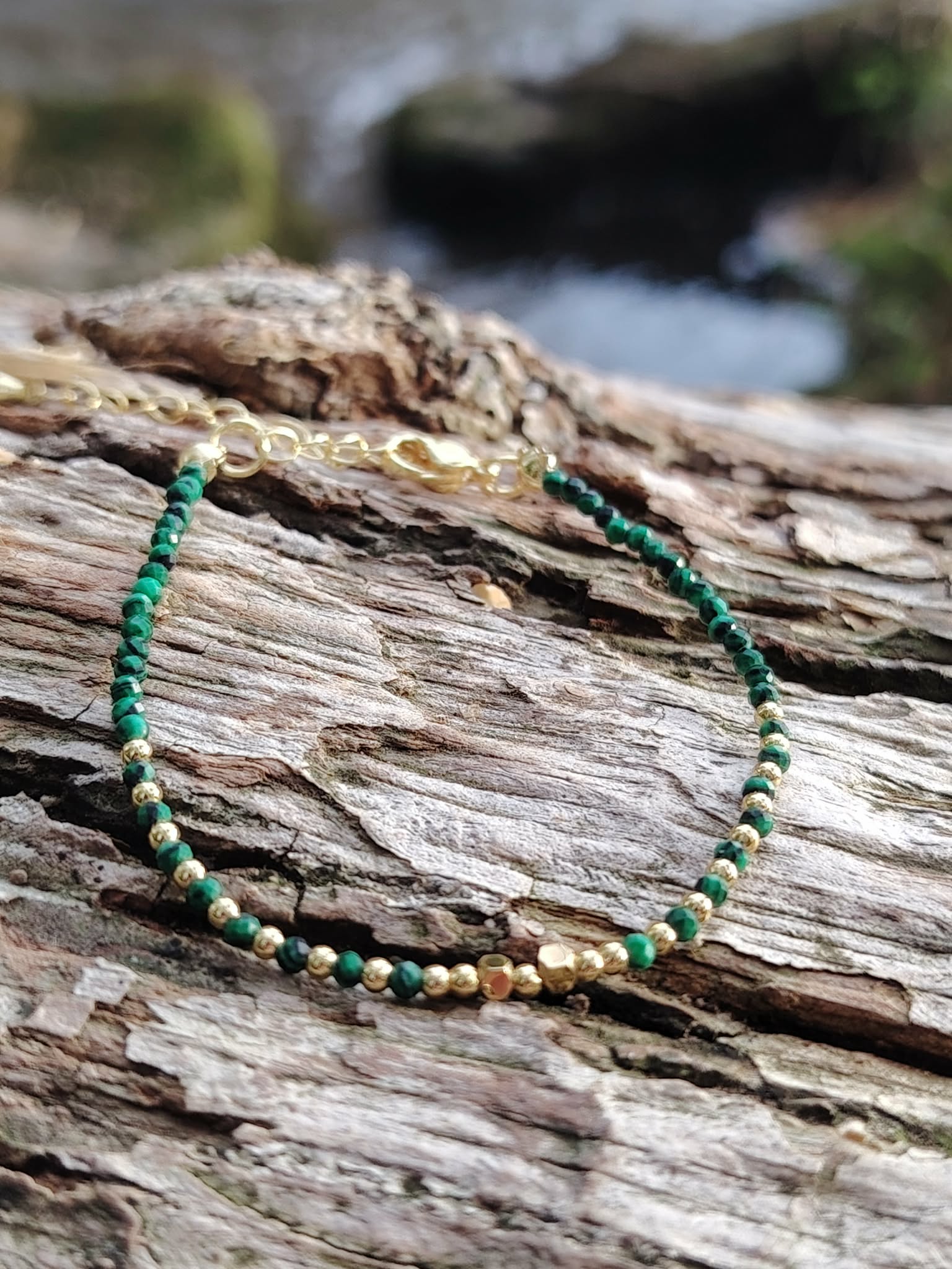 Bracelet malachite facettée 2 mm et cuivre plaqué or sur roche en Bretagne, perles vertes lumineuses avec mer floutée au fond