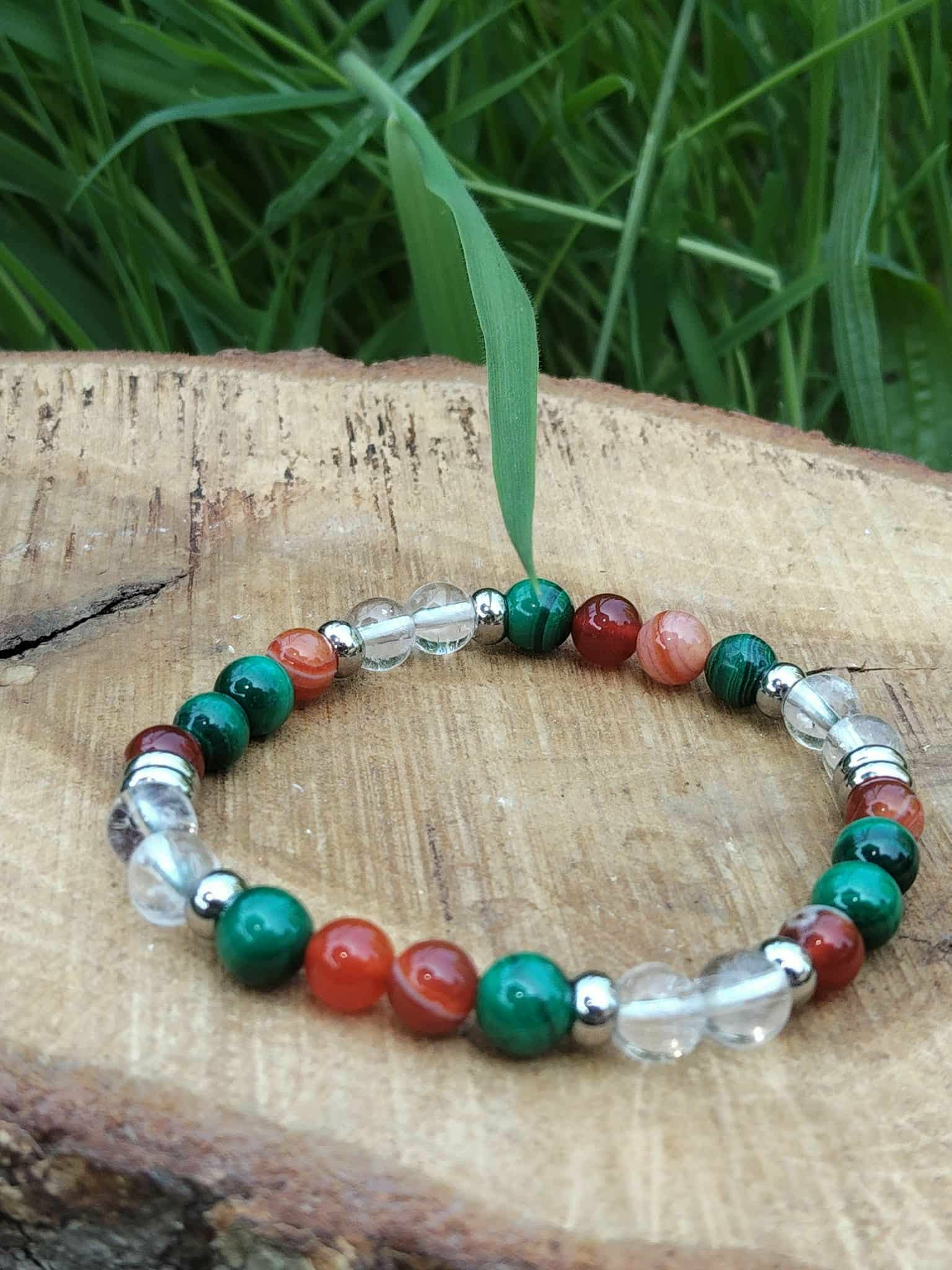 Bracelet prémenstruel 6 mm (malachite, cornaline, cristal de roche) posé sur pierre beige en extérieur, feuillage vert en arrière-plan, création Magic Gaïa; intention apaisement, équilibre émotionnel.