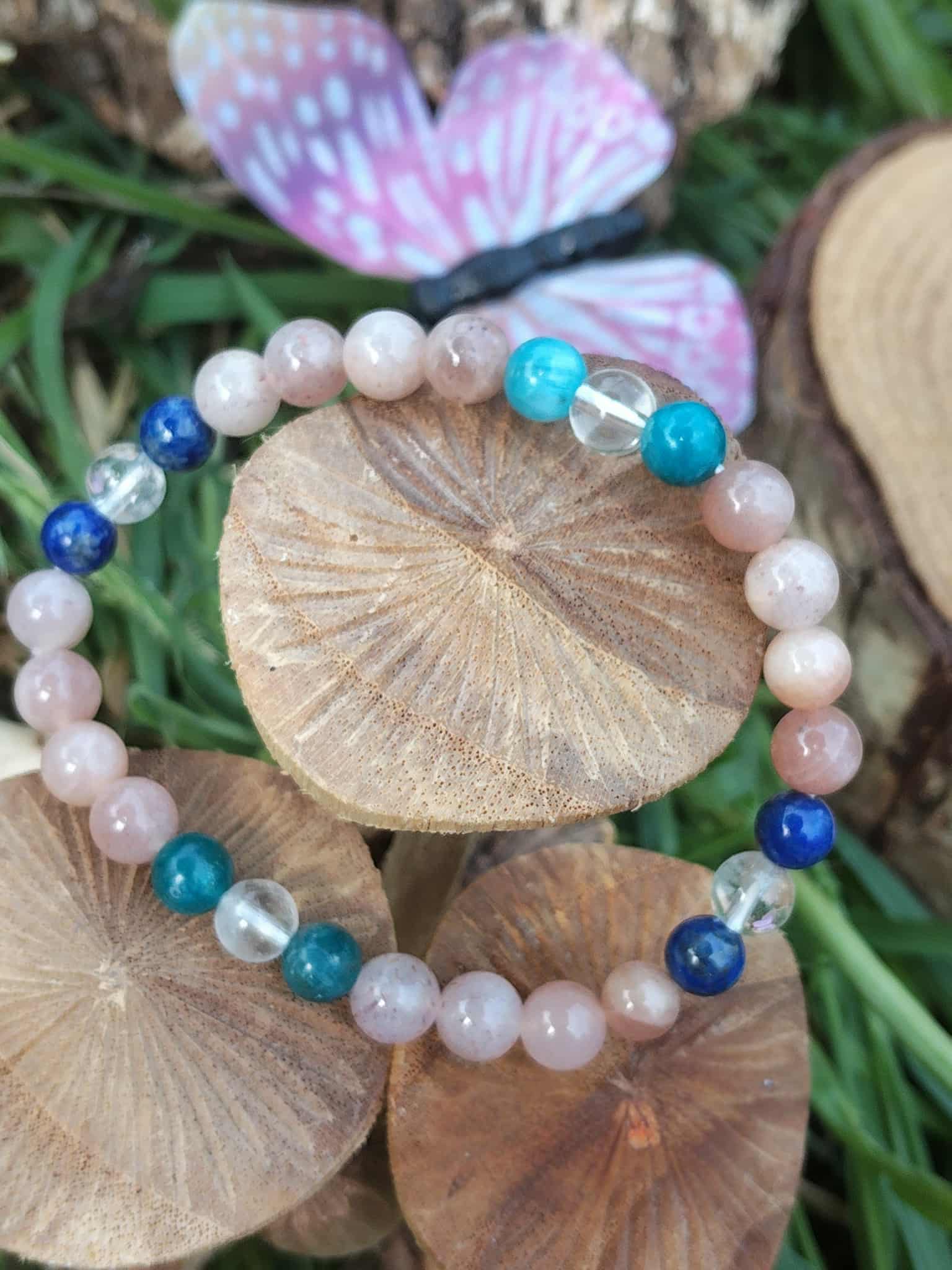 Bracelet bien-être en pierres naturelles photographié de biais sur bois brut, nuances pêche, bleu nuit et transparent pour assurance intérieure et rayonnement doux