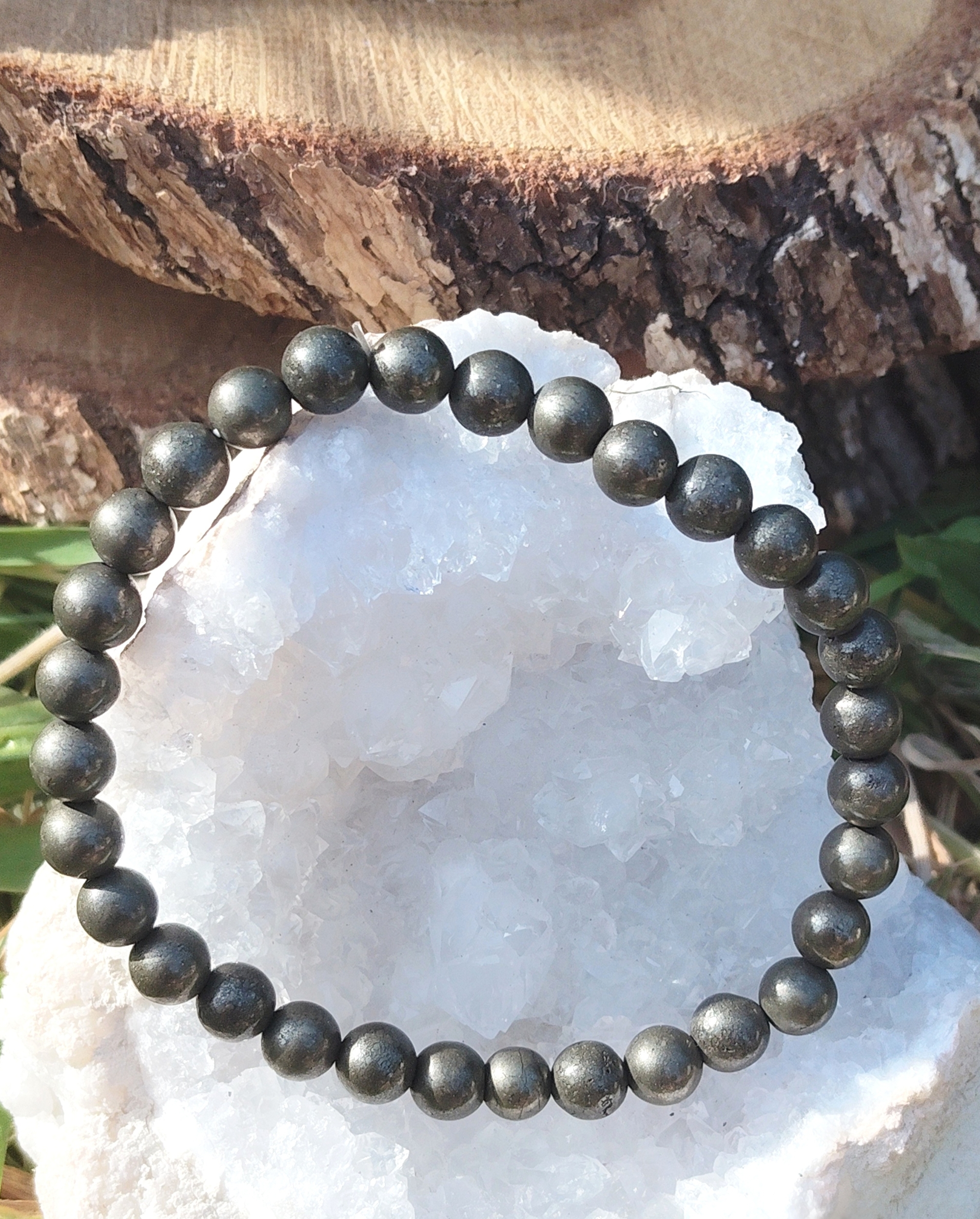 Bracelet pyrite 6 mm gris anthracite métallisé en perles rondes présenté sur un amas de quartz c, dans un décor minéral naturel, évoquant la solidité, la vigilance et la force intérieure