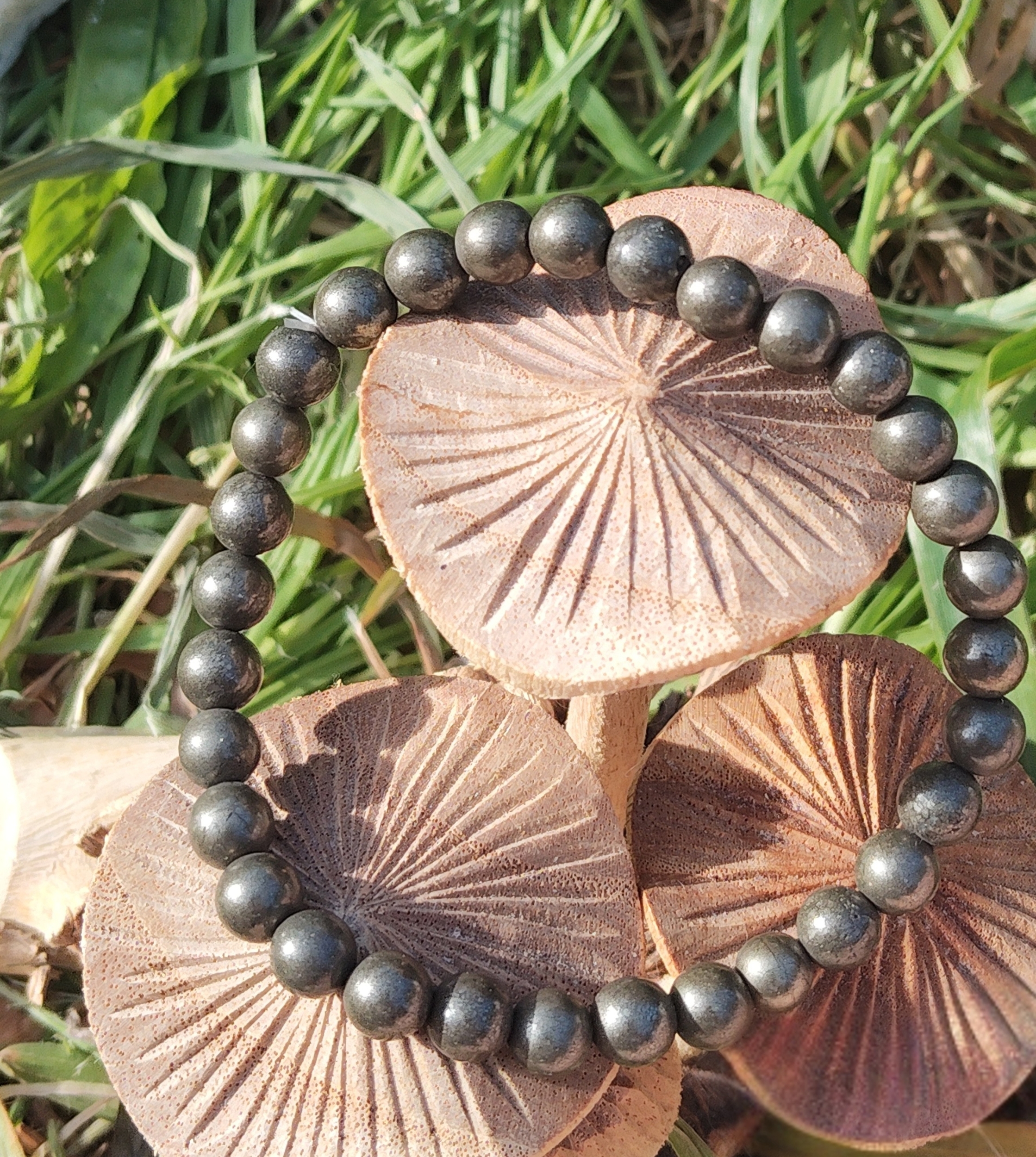 Bracelet pyrite 6 mm en perles rondes présenté sur des champignons décoratifs au milieu de l’herbe, évoquant la force mentale, la détermination et l’assurance intérieure