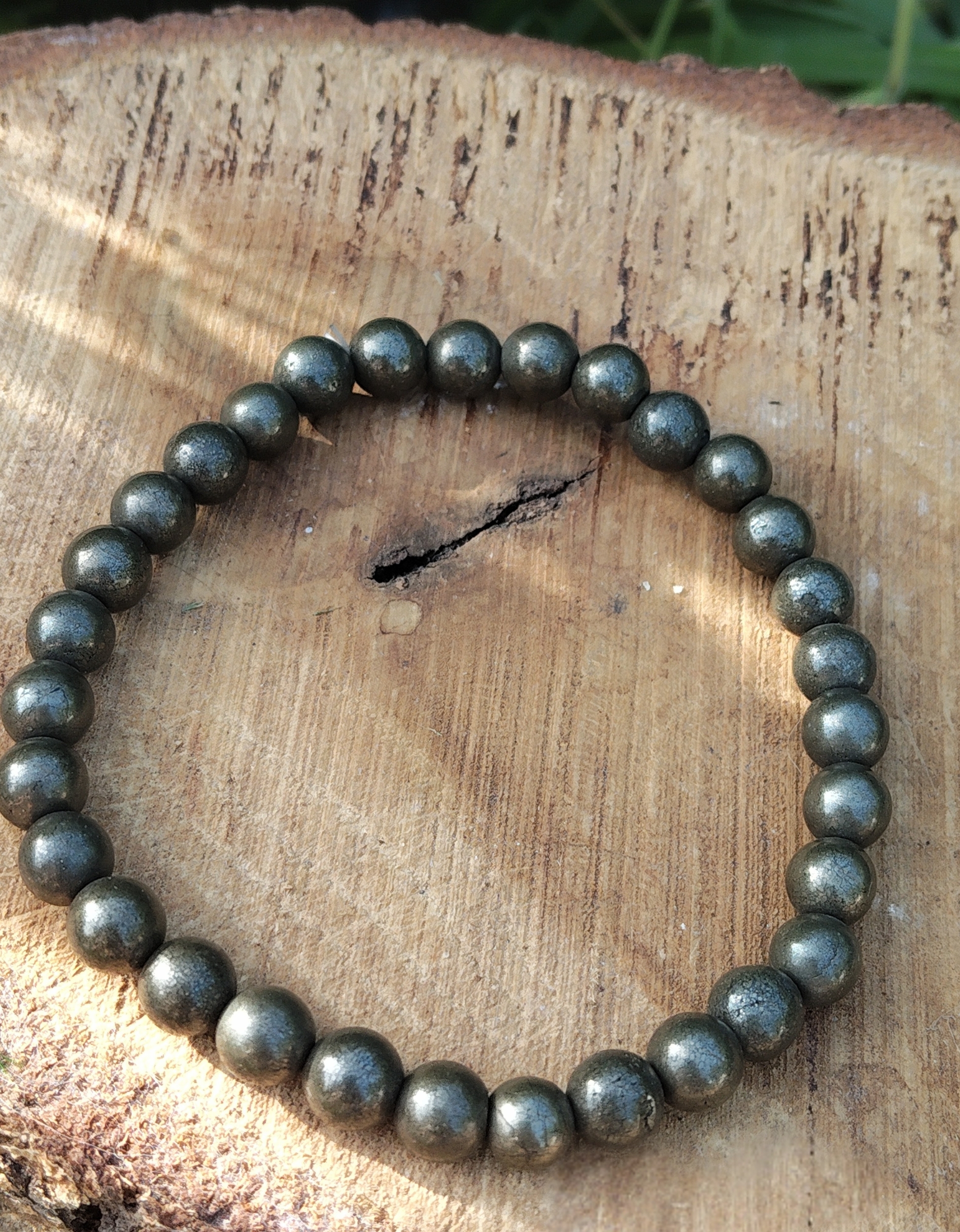 Bracelet pyrite 6 mm gris anthracite métallisé en perles rondes posé sur un support en bois, sous lumière naturelle, évoquant la concentration, la ténacité et l’ancrage mental