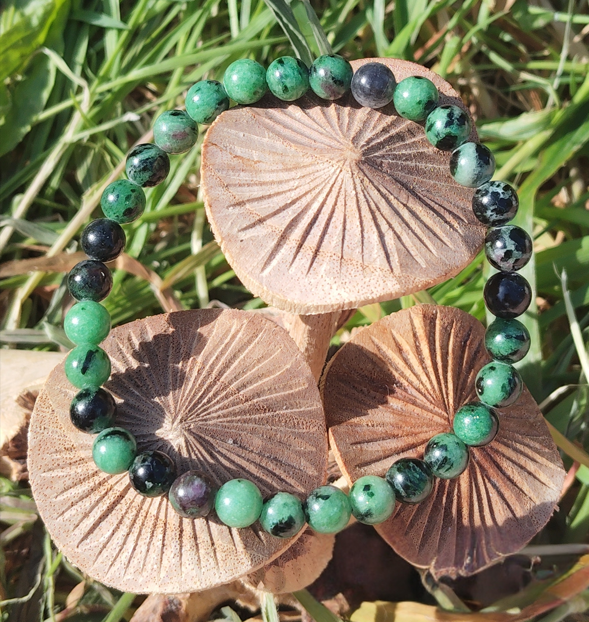 Bracelet rubis zoïsite en perles rondes sur champignons décoratifs dans l’herbe, créativité vivante, assurance personnelle et harmonie émotionnelle