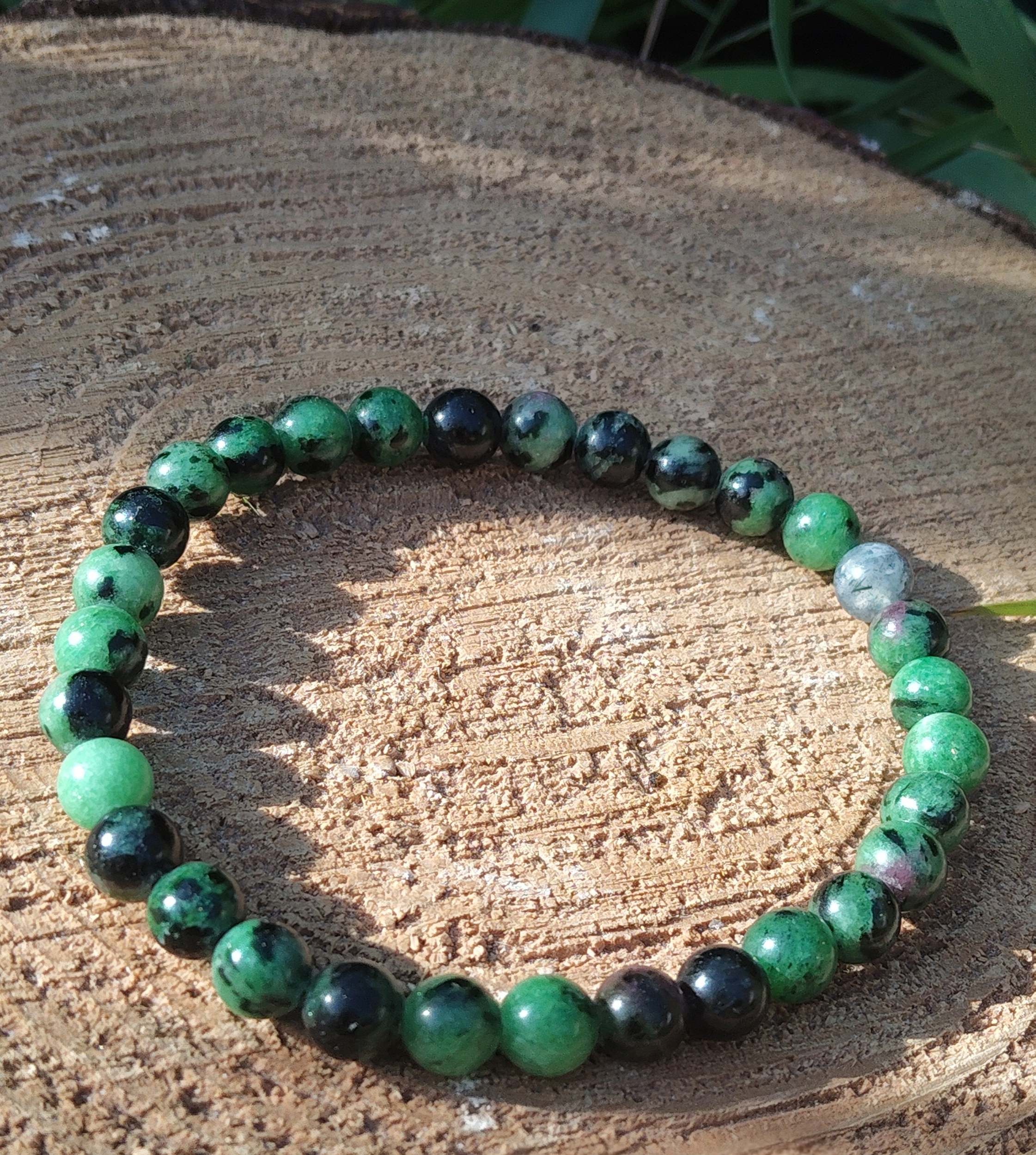Bracelet rubis zoïsite posé sur galet gravé et support en bois au soleil, expression authentique, énergie du cœur et motivation intérieure