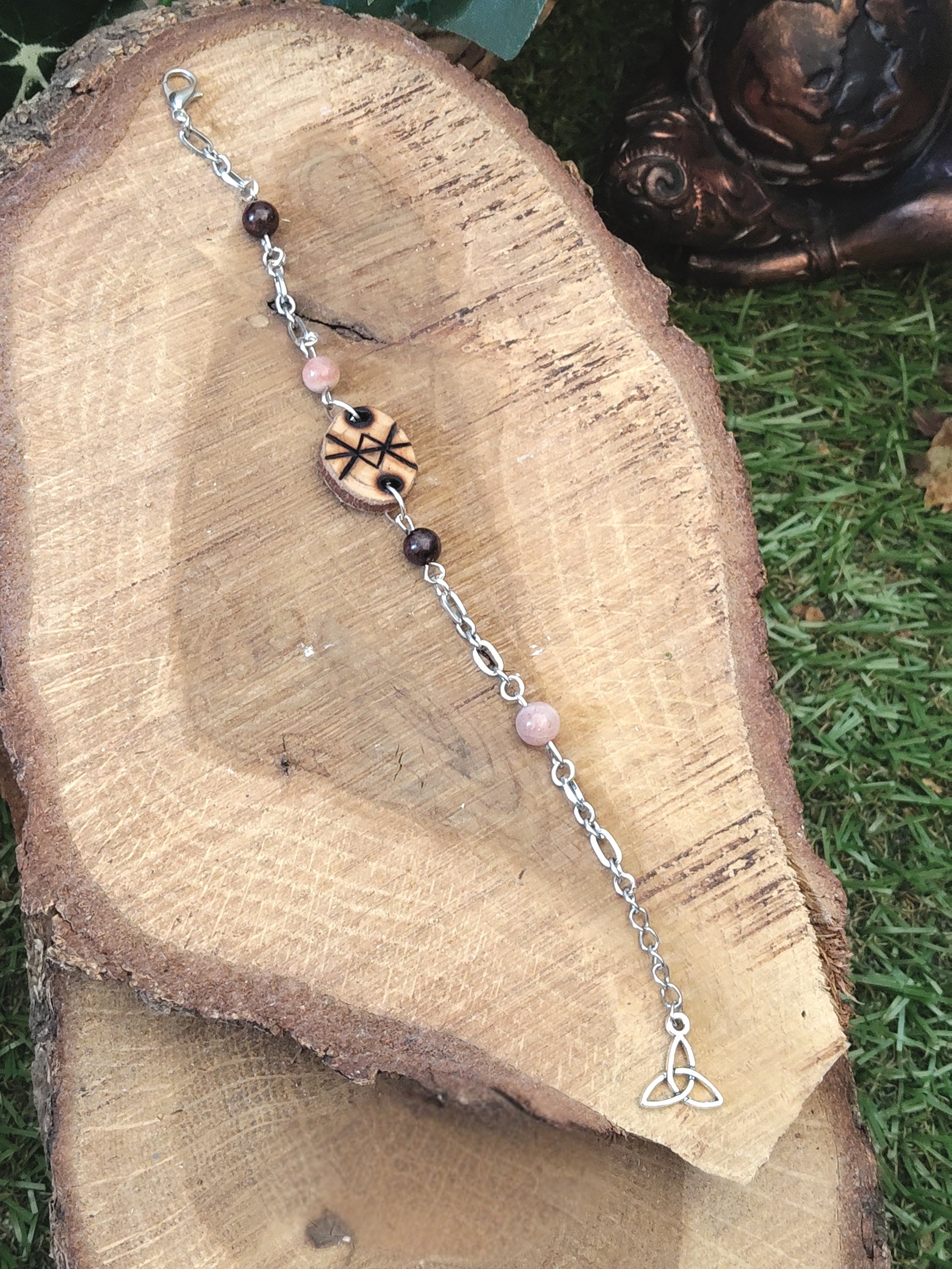 Bracelet rune de protection en bois création Magic Gaïa, chaîne argentée avec perles quartz rose et grenat, posé sur tranche de bois et herbe, intention: protection douce et apaisement