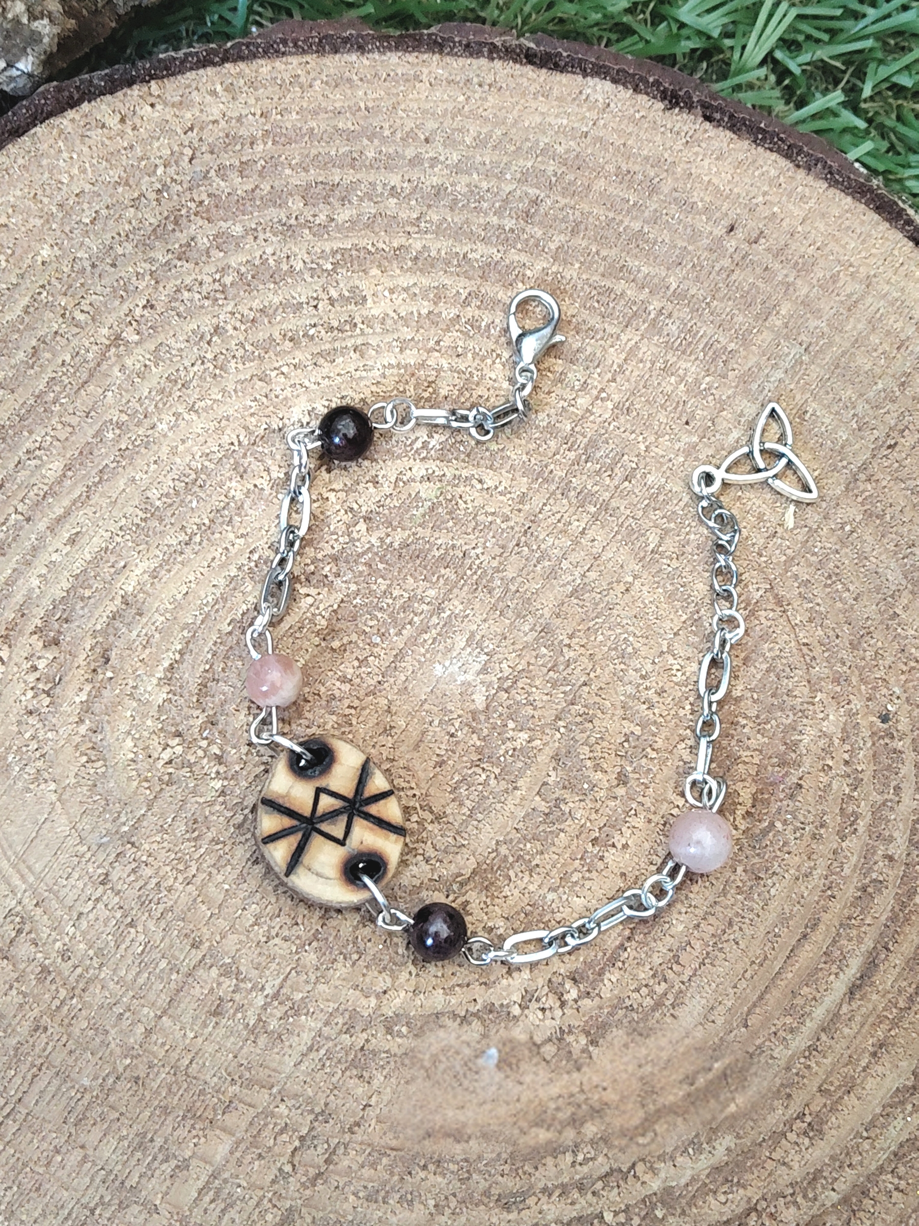 Bracelet rune de protection en bois Magic Gaïa, chaîne argentée avec perles quartz rose et grenat, posé sur rondin de bois, intention: apaisement et protection.