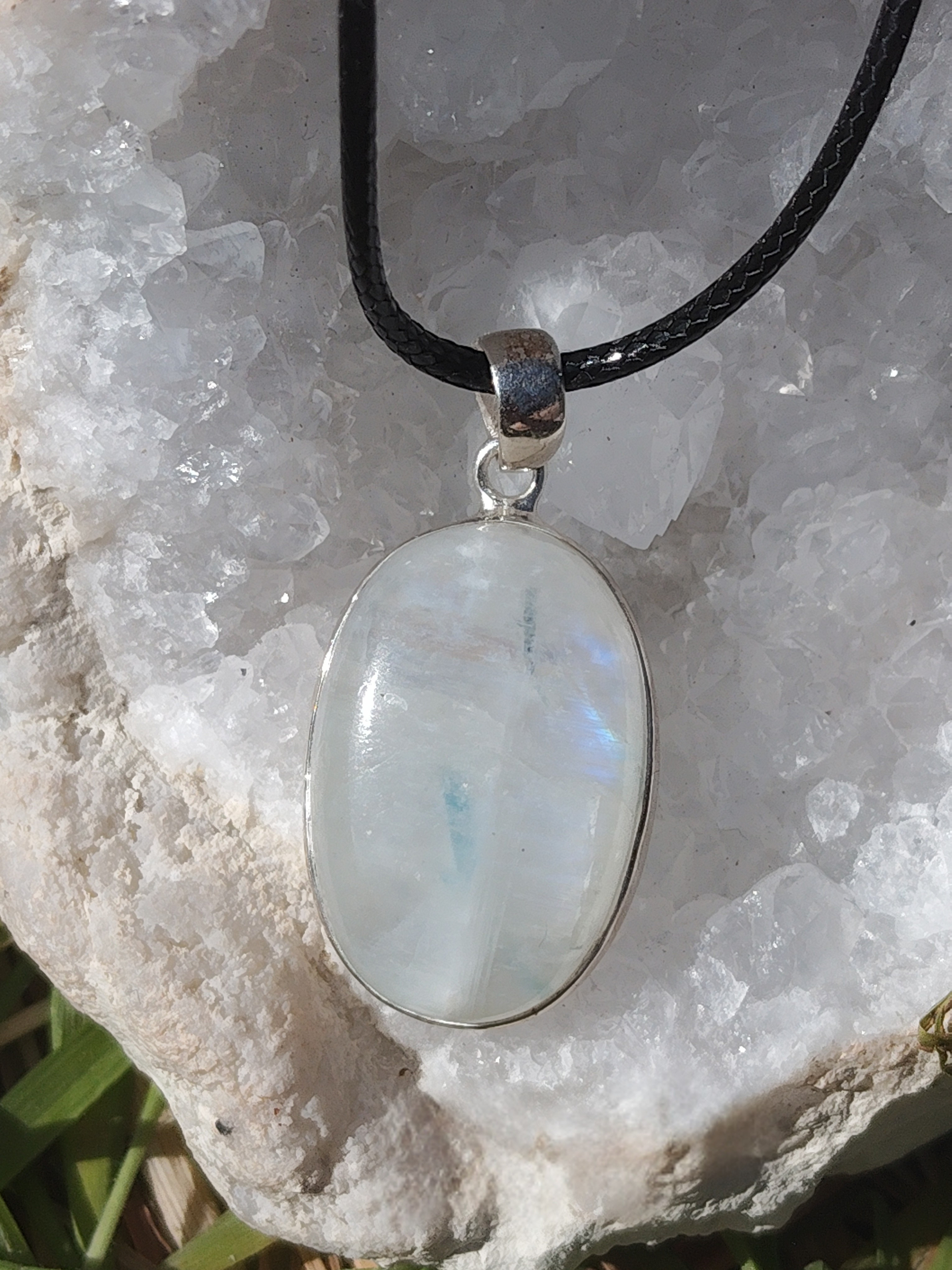 Pendentif labradorite blanche ovale sertie en argent 925 sur cordon noir, posé sur amas de quartz blanc en extérieur, pierre naturelle associée à l’intuition, à la douceur et à l’harmonie intérieure.