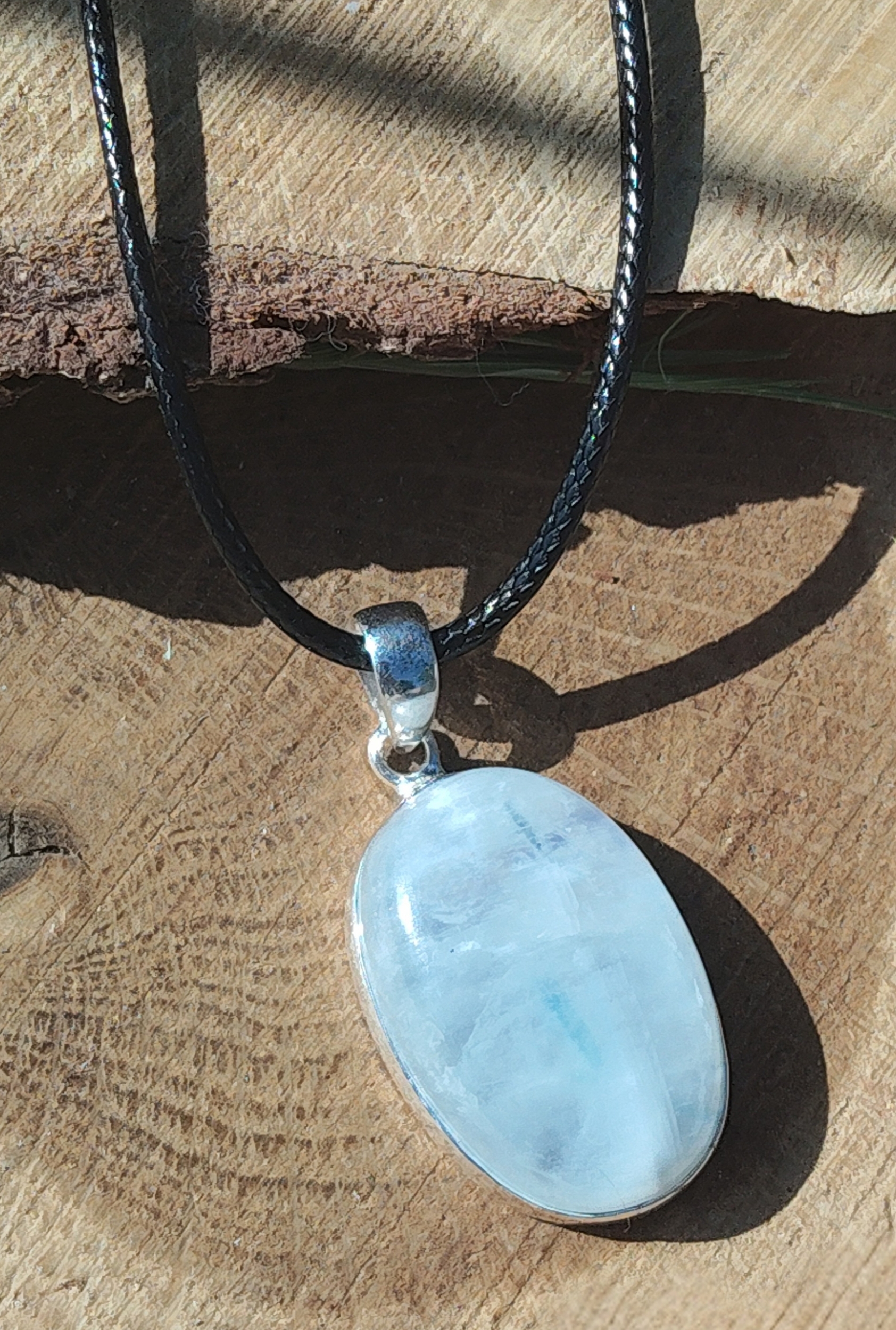 Pendentif labradorite blanche ovale en argent 925 sur cordon noir, posé sur rondin de bois au soleil, bijou en pierre naturelle associé à la lucidité, à la paix intérieure et à la douceur émotionnelle.