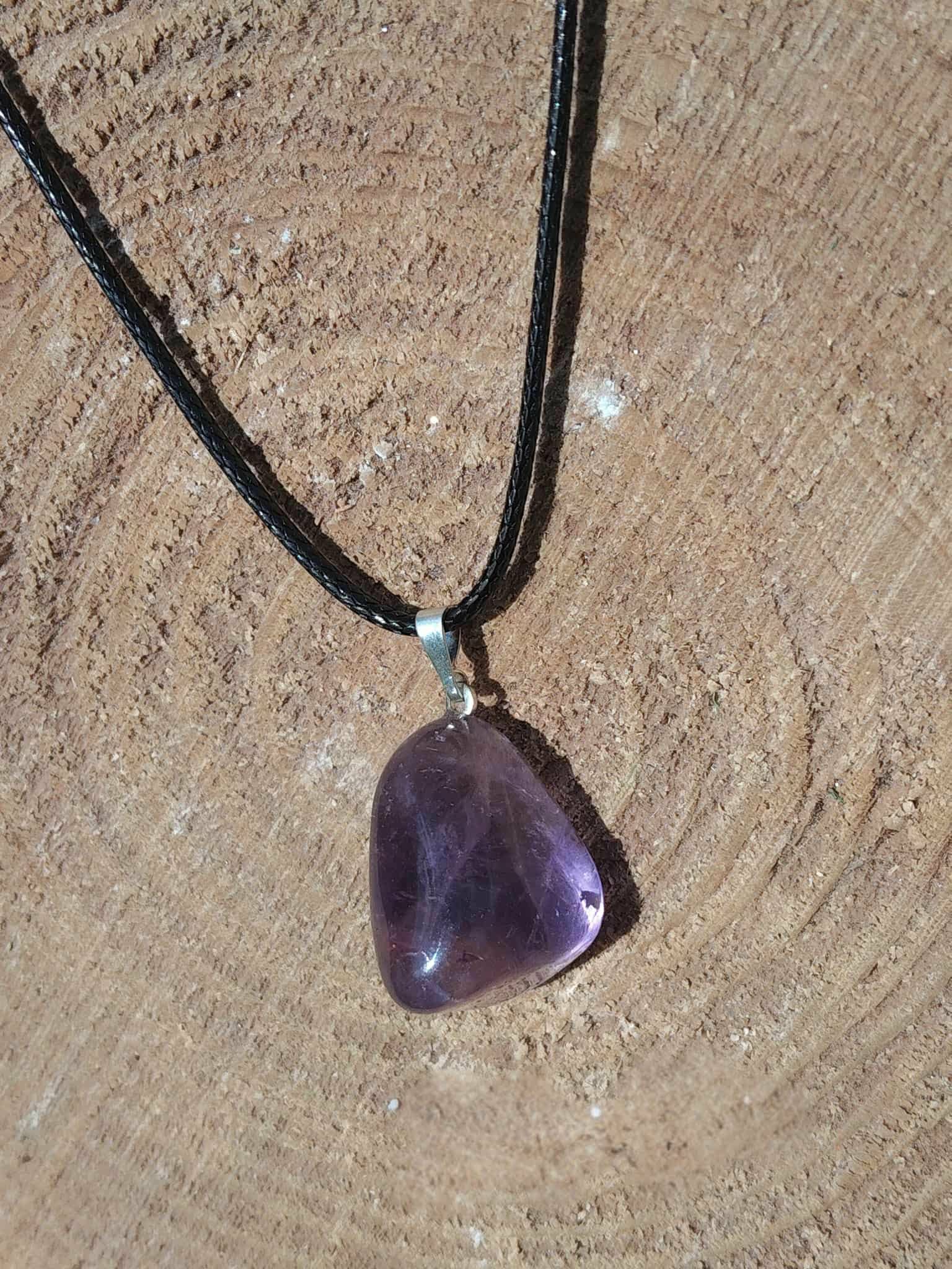 Pendentif en amétrine aux reflets violets sur cordon noir, présenté sur bois naturel, pierre naturelle évoquant l’inspiration, la tranquillité et la justesse intérieure.