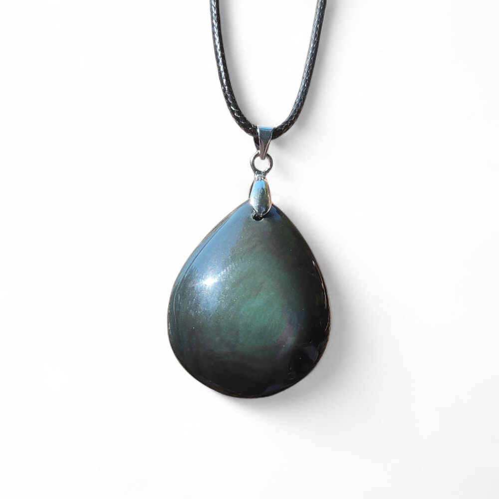 Pendentif goutte en obsidienne œil céleste aux reflets sombres sur cordon noir et bélière argentée, présenté sur fond clair, pierre naturelle reliée au recentrage, à la clairvoyance et à l’ancrage.
