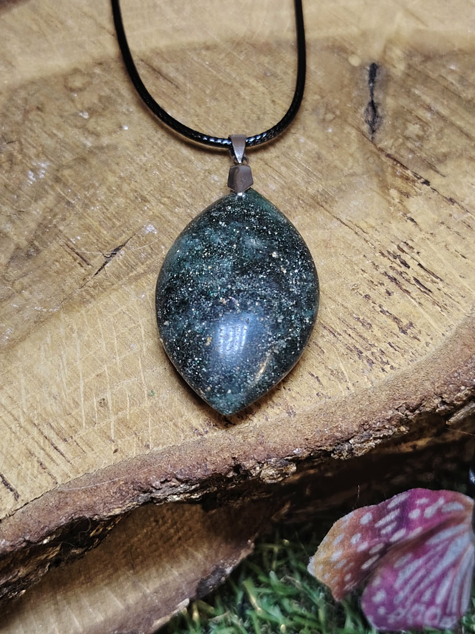 Pendentif en fuchsite avec inclusion de marcassite sur vieux grimoire, dans une ambiance ésotérique, évoquant clarté, harmonie et apaisement.