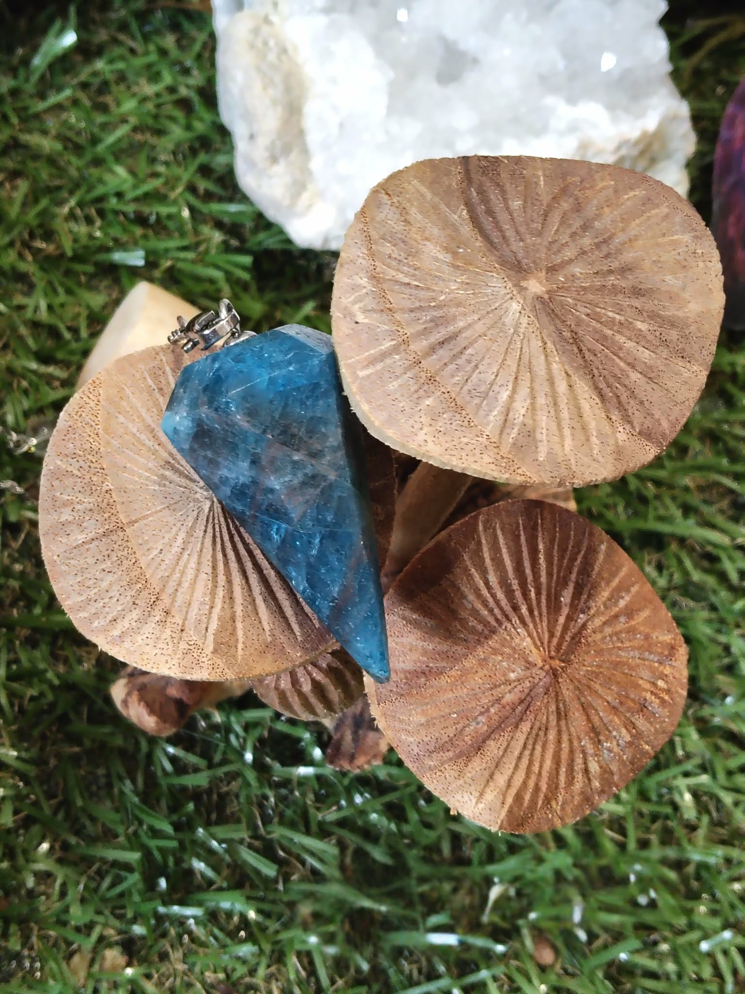 Pendule en apatite bleue posé parmi des champignons beiges sur mousse verte, dans un décor naturel et féerique, photo en extérieur, évoquant intuition, apaisement émotionnel et clarté intérieure