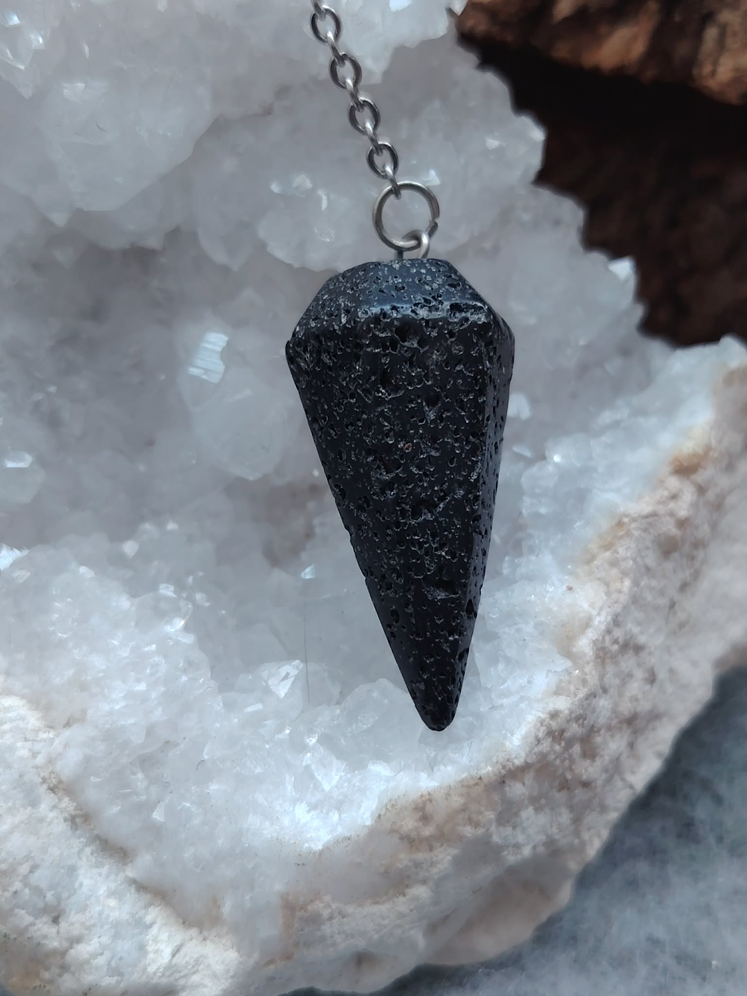Pendule en pierre de lave noire présenté sur un amas de quartz blanc dans un décor minéral naturel, une mise en scène évoquant ancrage, stabilité et recentrage.