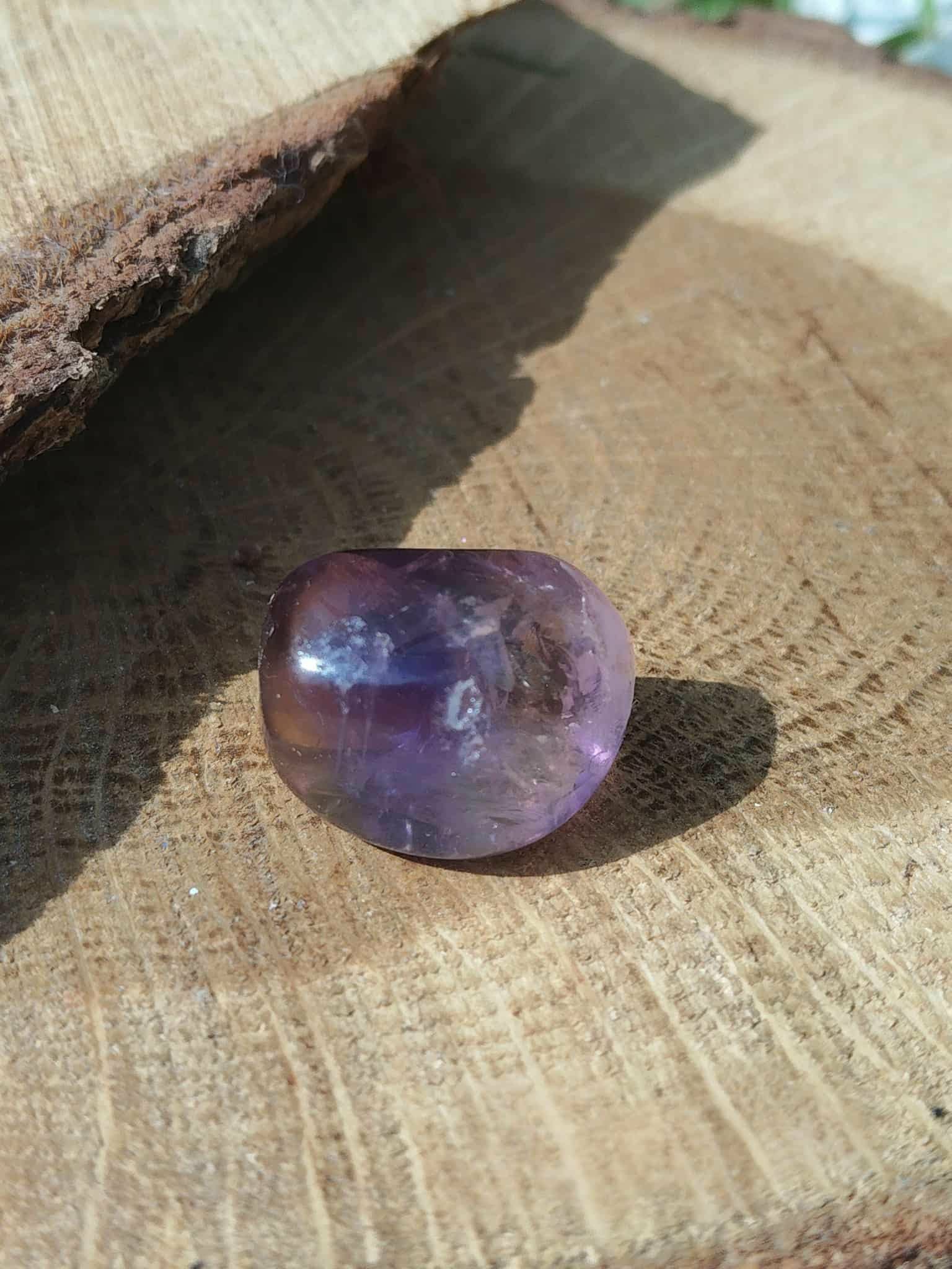 Pierre roulée d’amétrine aux reflets violets sur bois naturel, dans un décor chaleureux, pierre naturelle évoquant la présence à soi, la sérénité et la clarté d’esprit.
