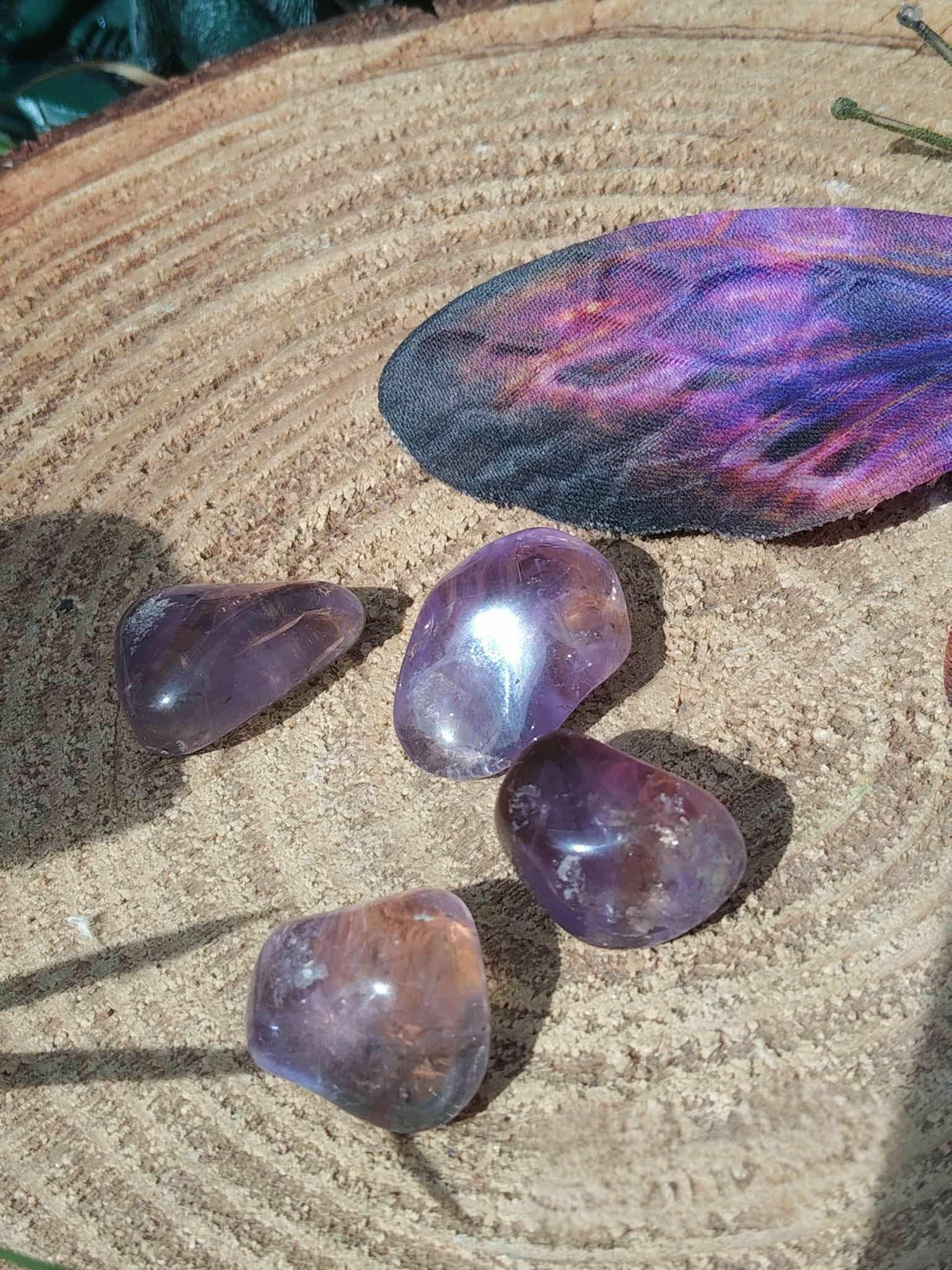 Pierres roulées d’amétrine aux reflets violets sur rondin de bois avec plume colorée, pierres naturelles évoquant la finesse d’esprit, la douceur intérieure et le recentrage.