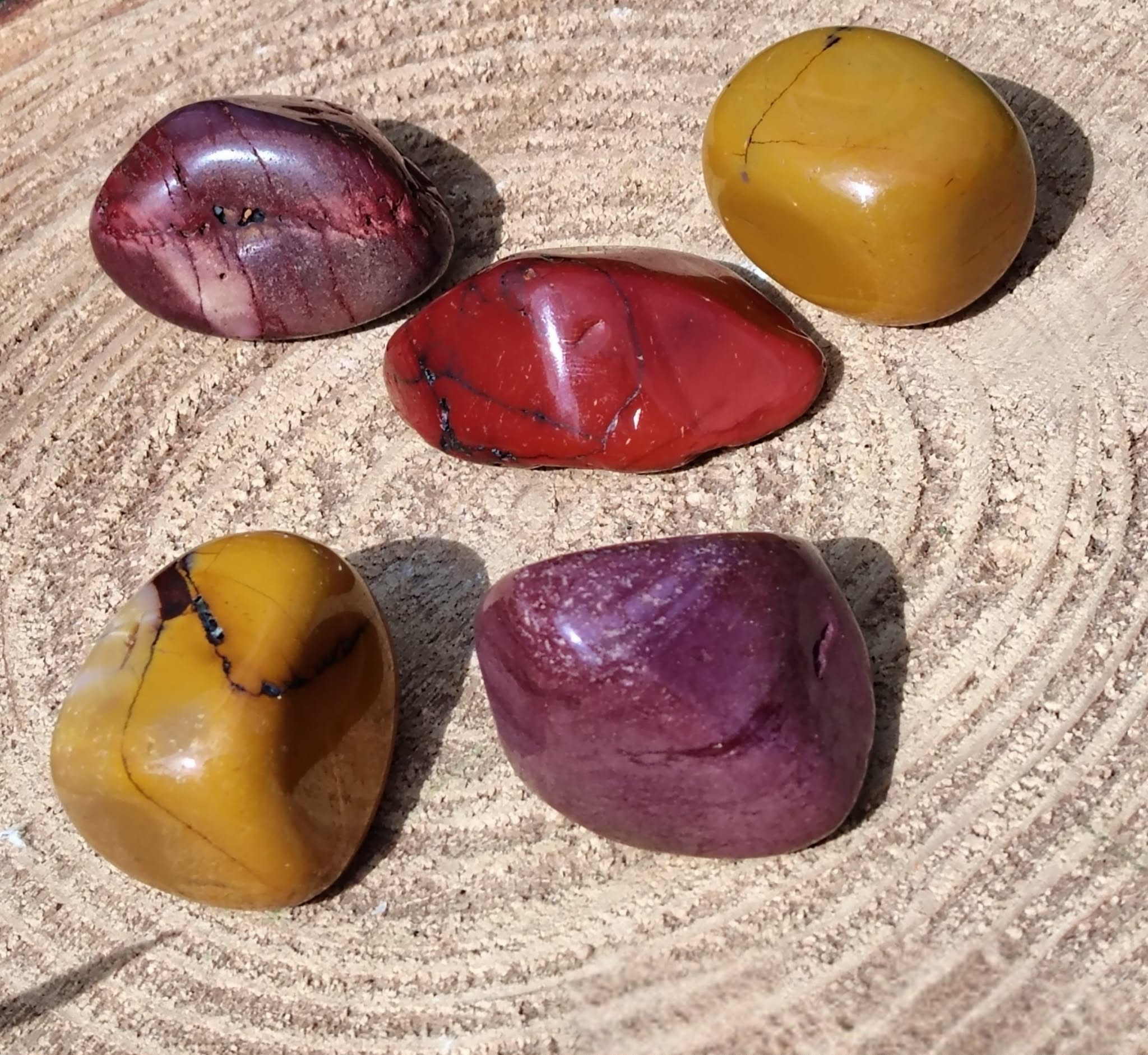 Pierres roulées de jaspe mookaïte aux teintes jaunes, rouges et bordeaux sur support en bois sculpté, pierres naturelles associées à l’élan vital, à la solidité émotionnelle et à l’assurance