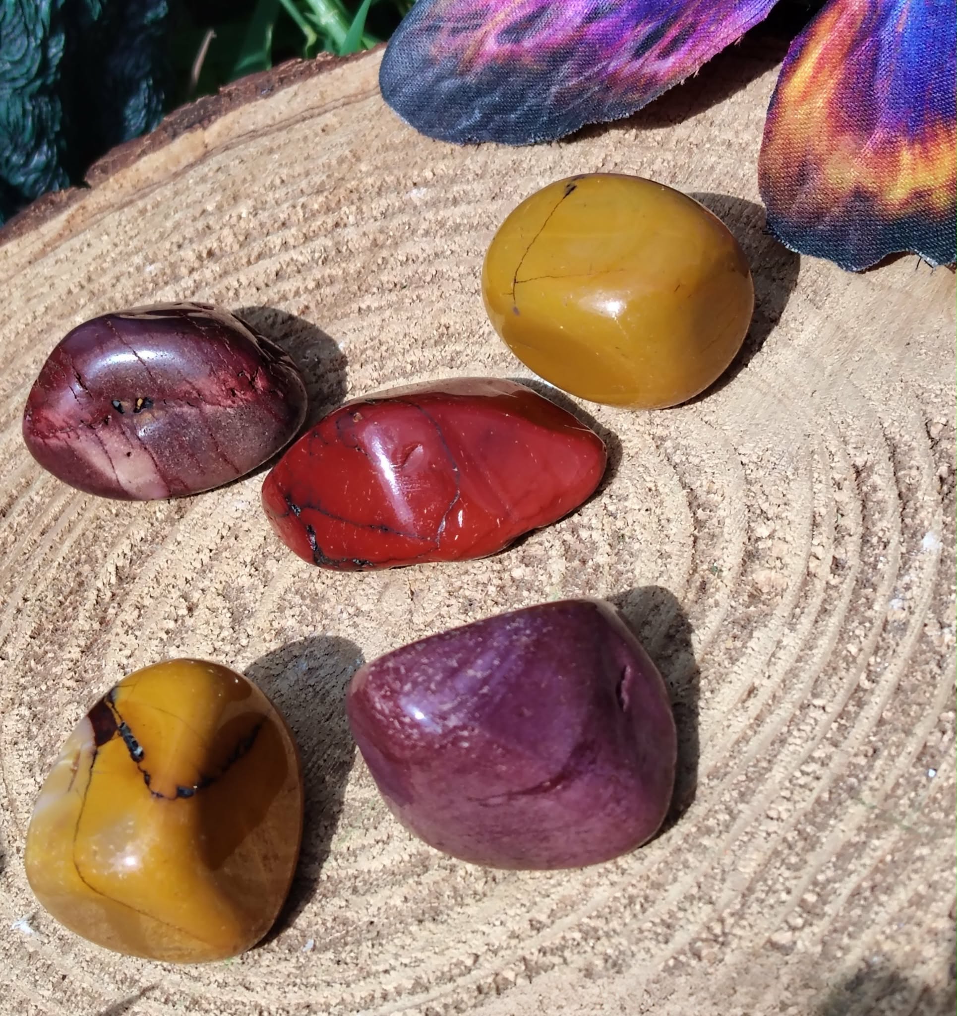 Pierres roulées de jaspe mookaïte disposées sur un support en bois sculpté, en lumière chaude naturelle, pierres naturelles reliées à l’enracinement, à la force douce et à la présence à soi.