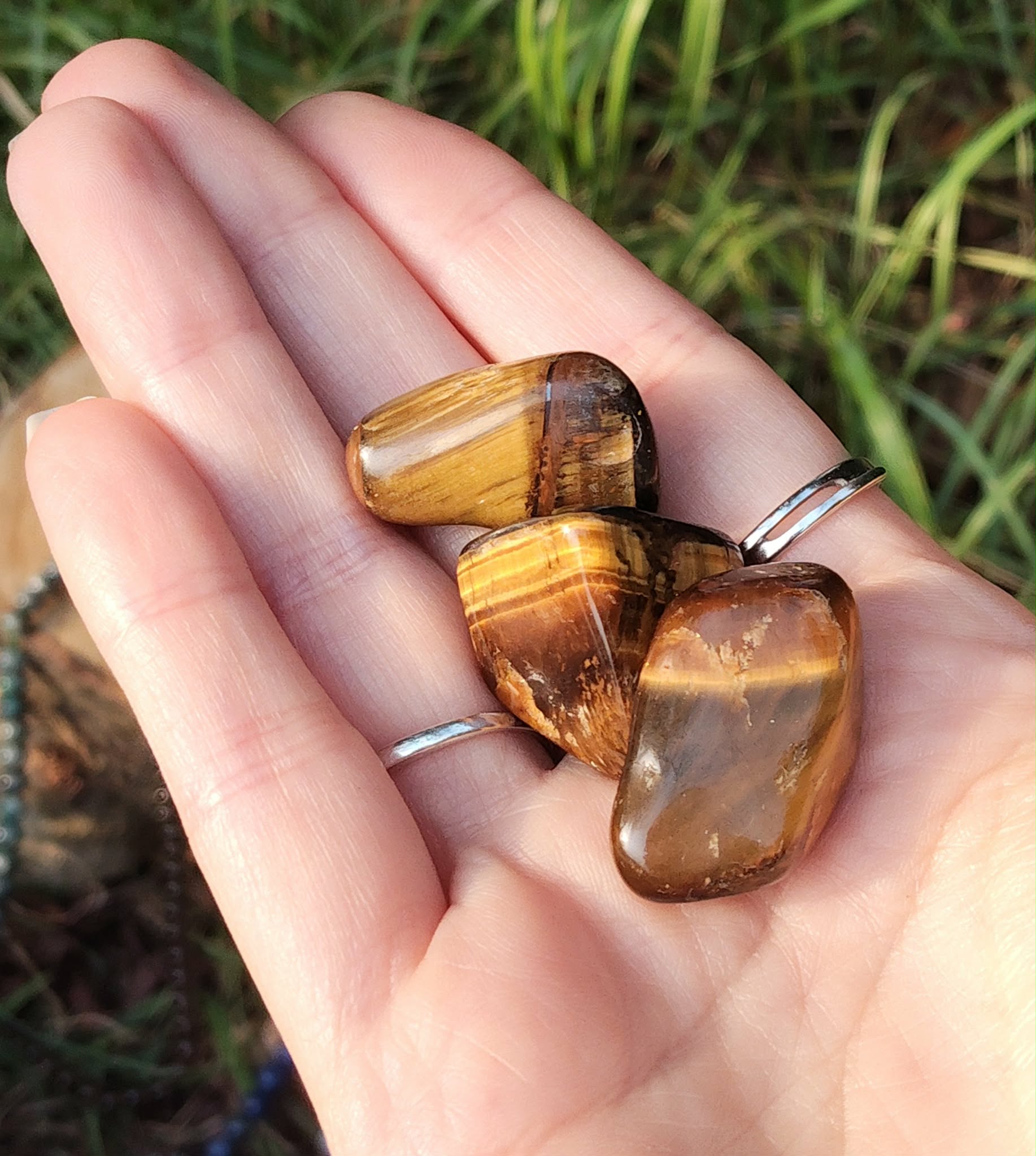 Trois pierres roulées œil de tigre aux reflets dorés reposent dans une main, pierres naturelles reliées à la volonté, au recentrage et à la confiance calme.