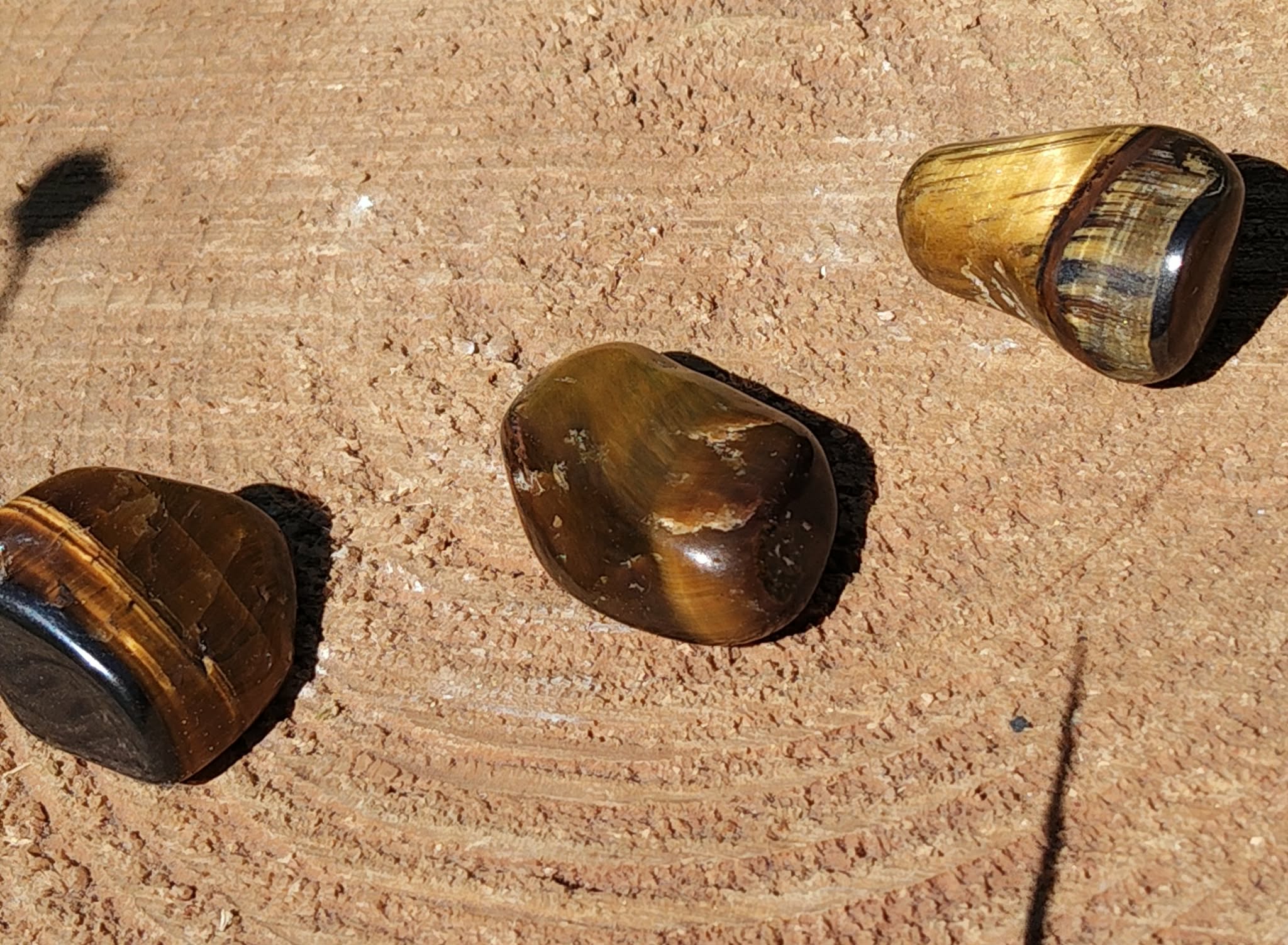 Trois pierres roulées œil de tigre aux tons bruns et dorés disposées sur une surface naturelle, pierres naturelles associées à la constance, à la fermeté intérieure et à l’équilibre émotionnel.