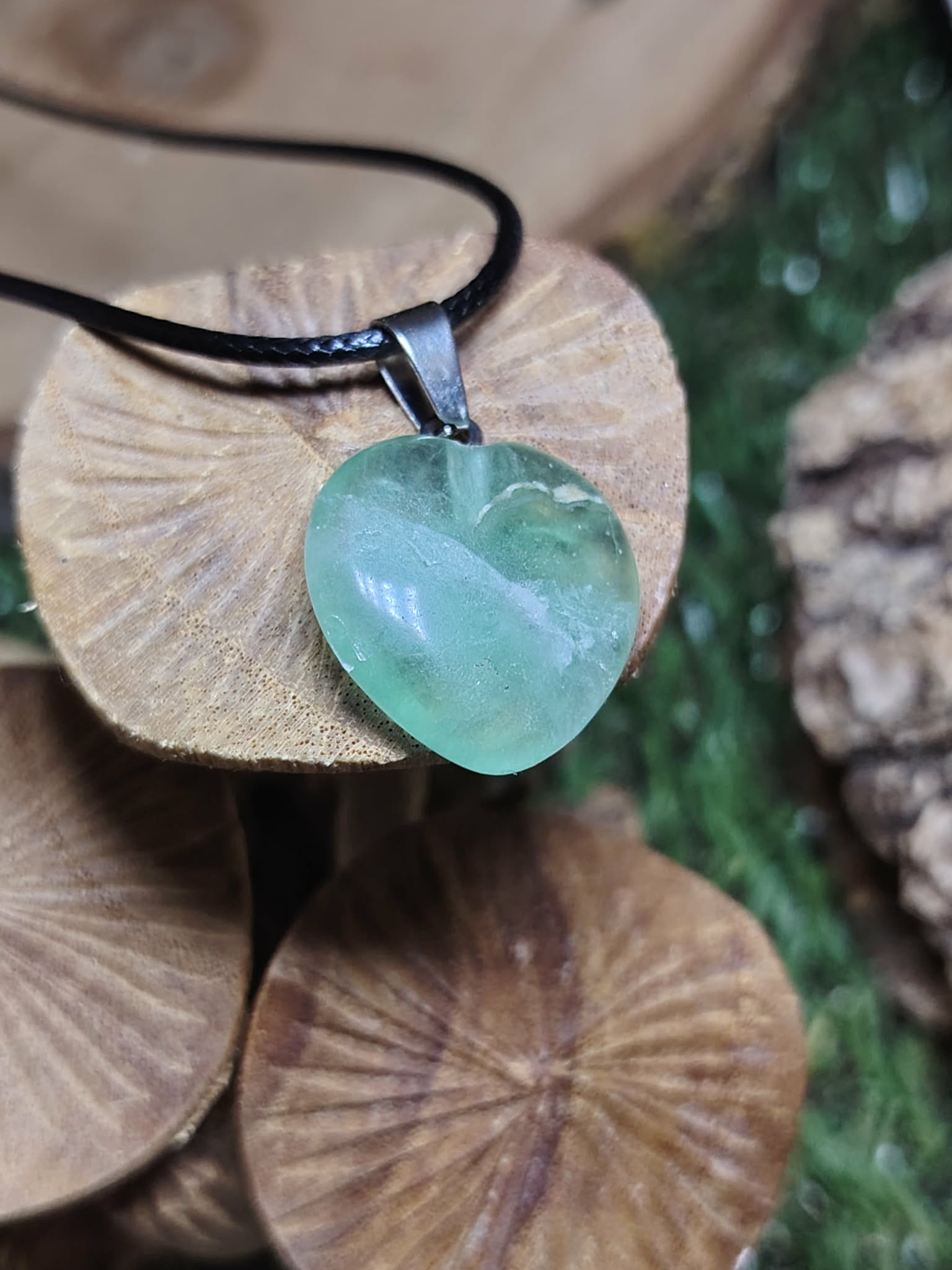 Pendentif cœur en fluorite multicolore aux reflets bleu-vert, posé sur des rondelles de bois, symbole d’apaisement, de clarté mentale et d’équilibre émotionnel.