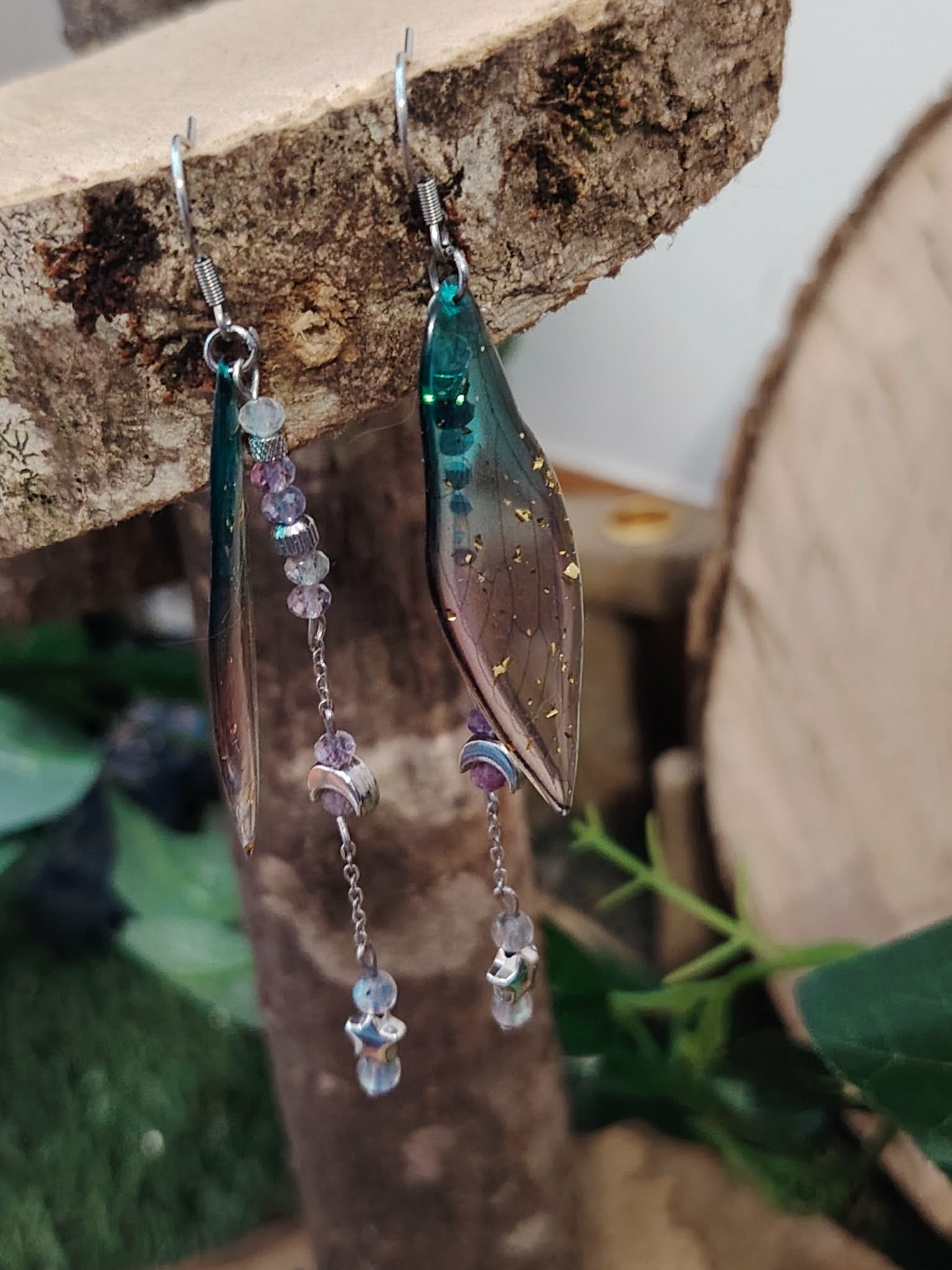 Boucles d’oreilles fée création Magic Gaïa suspendues à une écorce, ailes translucides vertes, chaînettes argentées et perles claires, sur fond doux naturel, pour une touche poétique, légère et féerique.