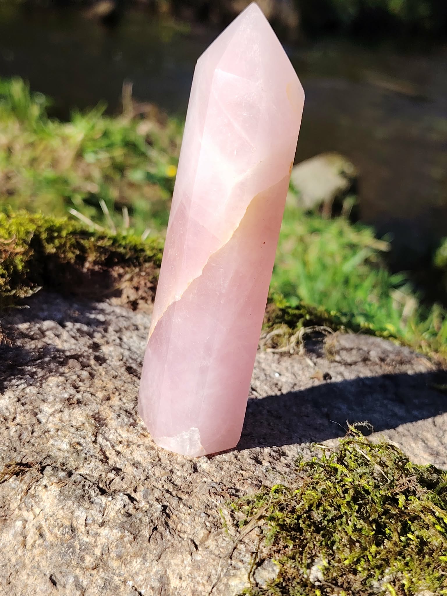 Pointe de quartz rose facettée dressée sur granit et mousse en Bretagne, près d’un ruisseau, pour apaiser le cœur, adoucir les émotions et encourager l’amour de soi.