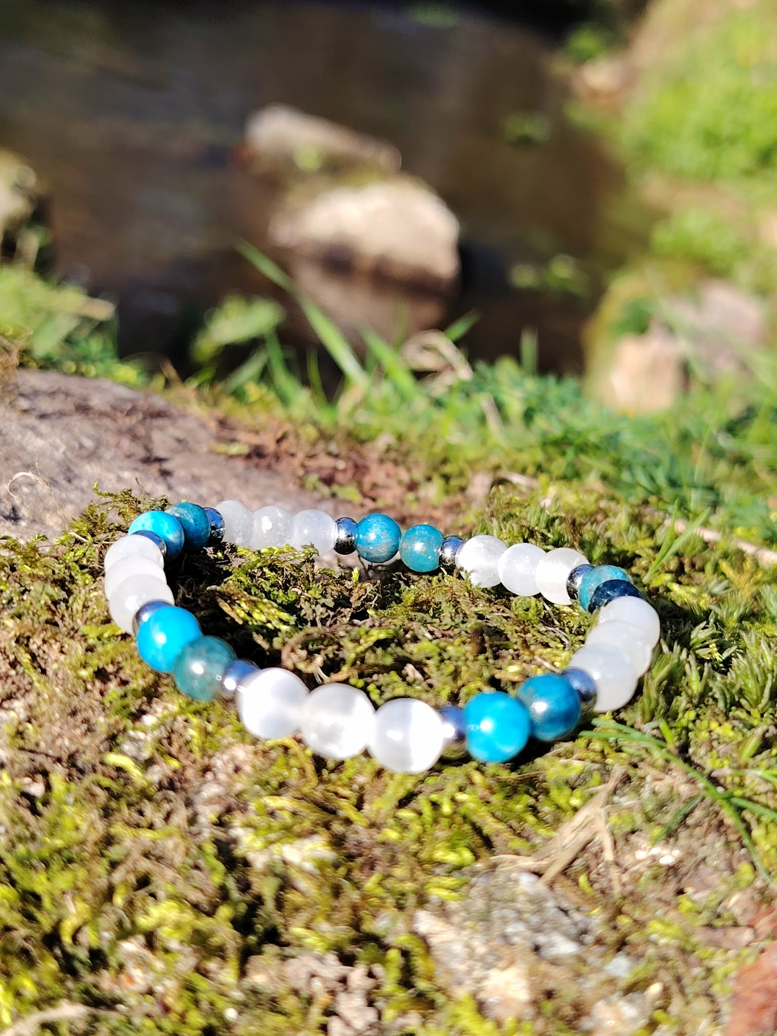 Bracelet TDAH création Magic Gaïa posé sur tapis de mousse en Bretagne avec rocher flou, apatite et sélénite pour apaiser la dispersion et soutenir l’attention