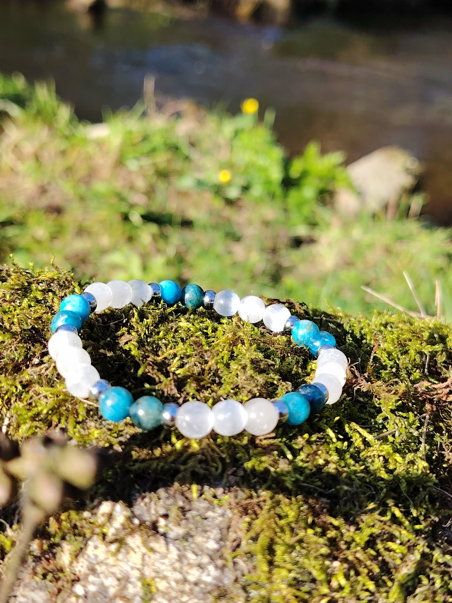 Bracelet TDAH création Magic Gaïa en apatite et sélénite sur rocher moussu en Bretagne, perles bleues et blanches pour canaliser l’agitation et retrouver un axe plus stable