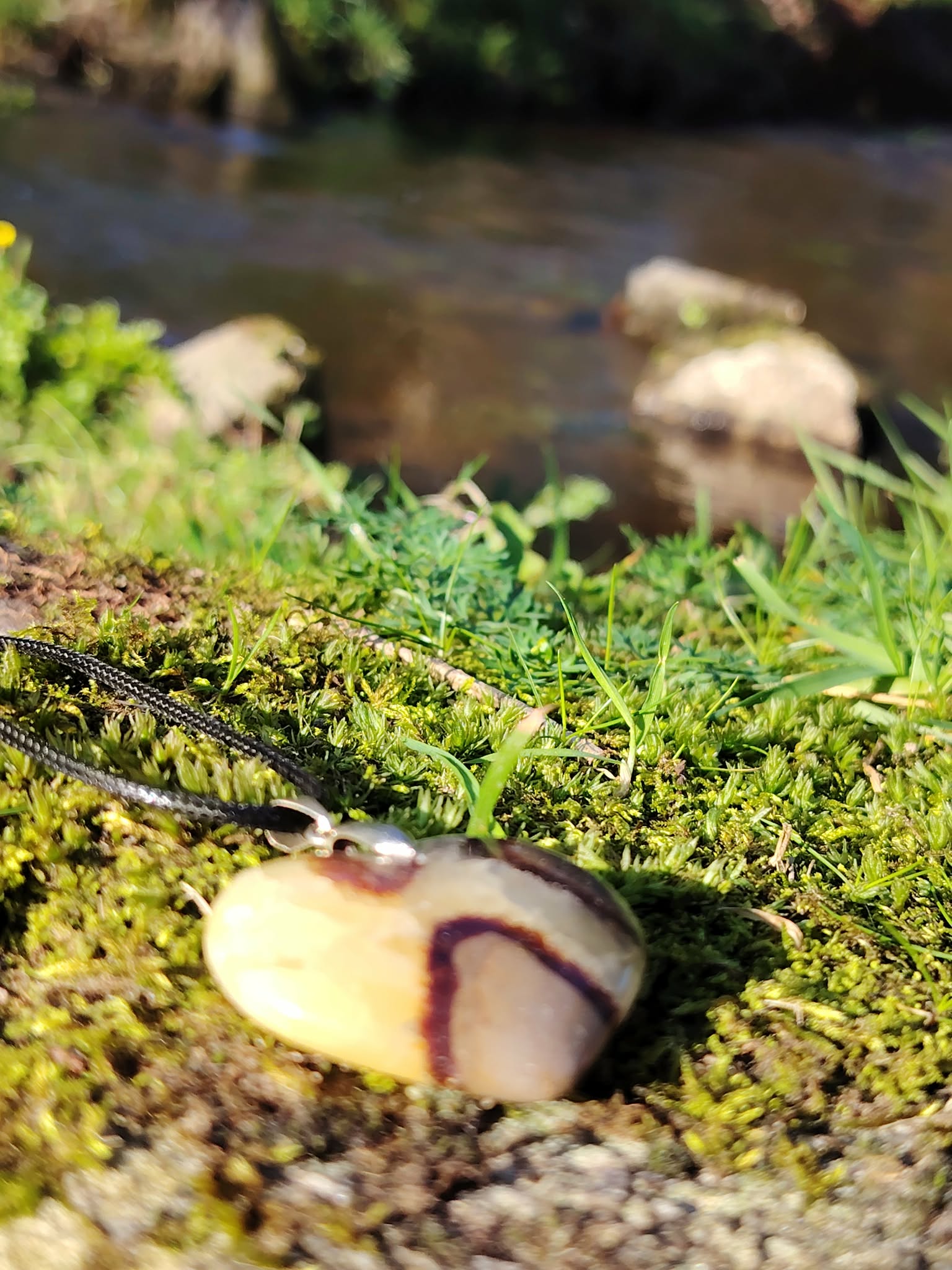 Pendentif cœur en septaria posé sur mousse près d’un ruisseau en forêt bretonne, pierre naturelle évoquant la sérénité, l’enracinement et l’harmonie intérieure.