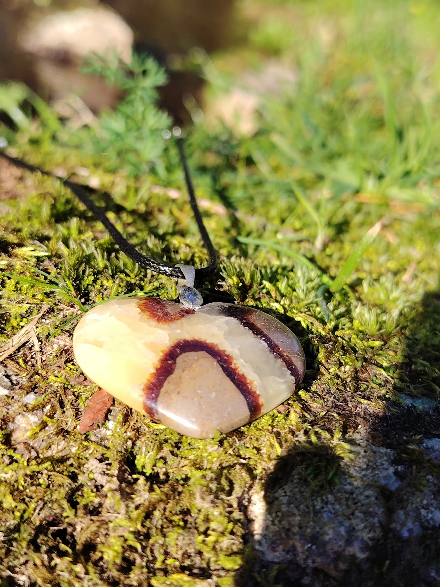 Pendentif cœur en septaria suspendu au-dessus de la mousse en forêt bretonne, dans une lumière naturelle chaleureuse, pierre naturelle associée à la confiance paisible, à l’ancrage et à la stabilité intérieure.