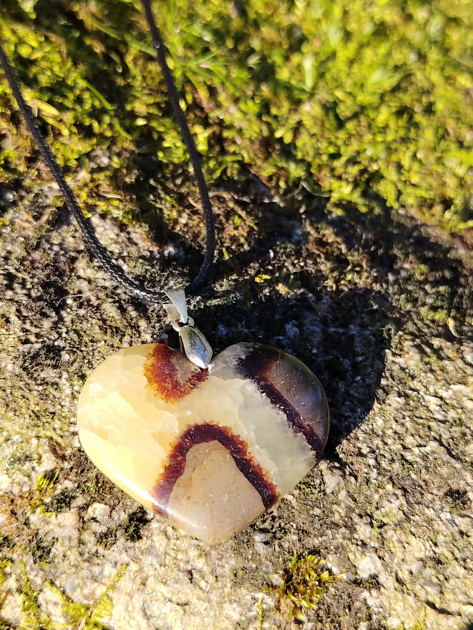 Pendentif cœur en septaria suspendu devant la mousse de forêt bretonne, sous une lumière dorée, pierre naturelle évoquant le recentrage, la force tranquille et l’équilibre intérieur.