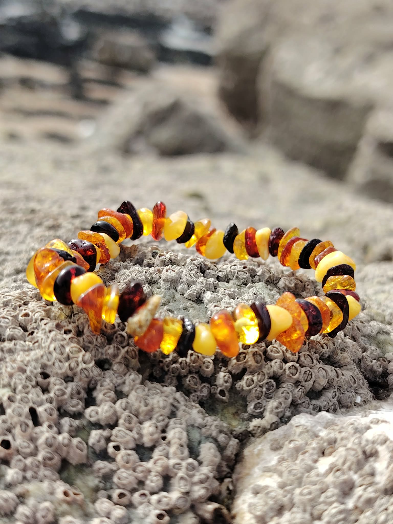 Bracelet ambre enfant baroque sur rocher granitique en Bretagne, éclats miel et cognac, sérénité, cocon rassurant et douceur affective