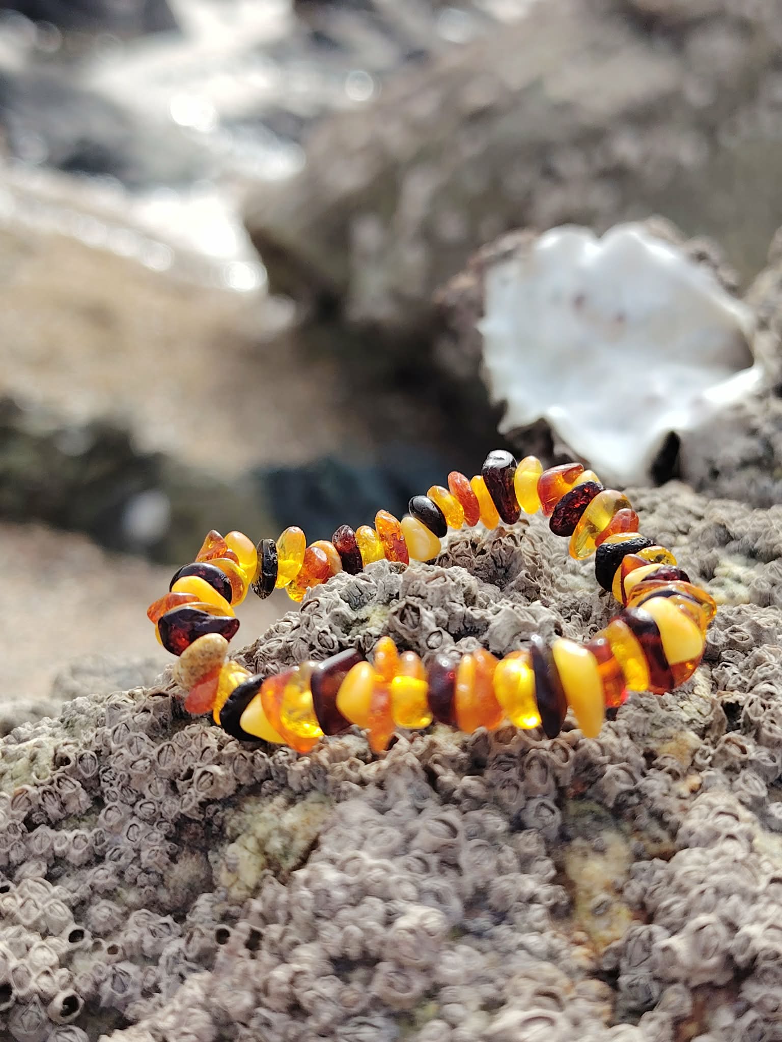 Bracelet ambre enfant sur rocher breton avec mer floue en arrière-plan, perles miel-cognac, détente émotionnelle et chaleur enveloppante