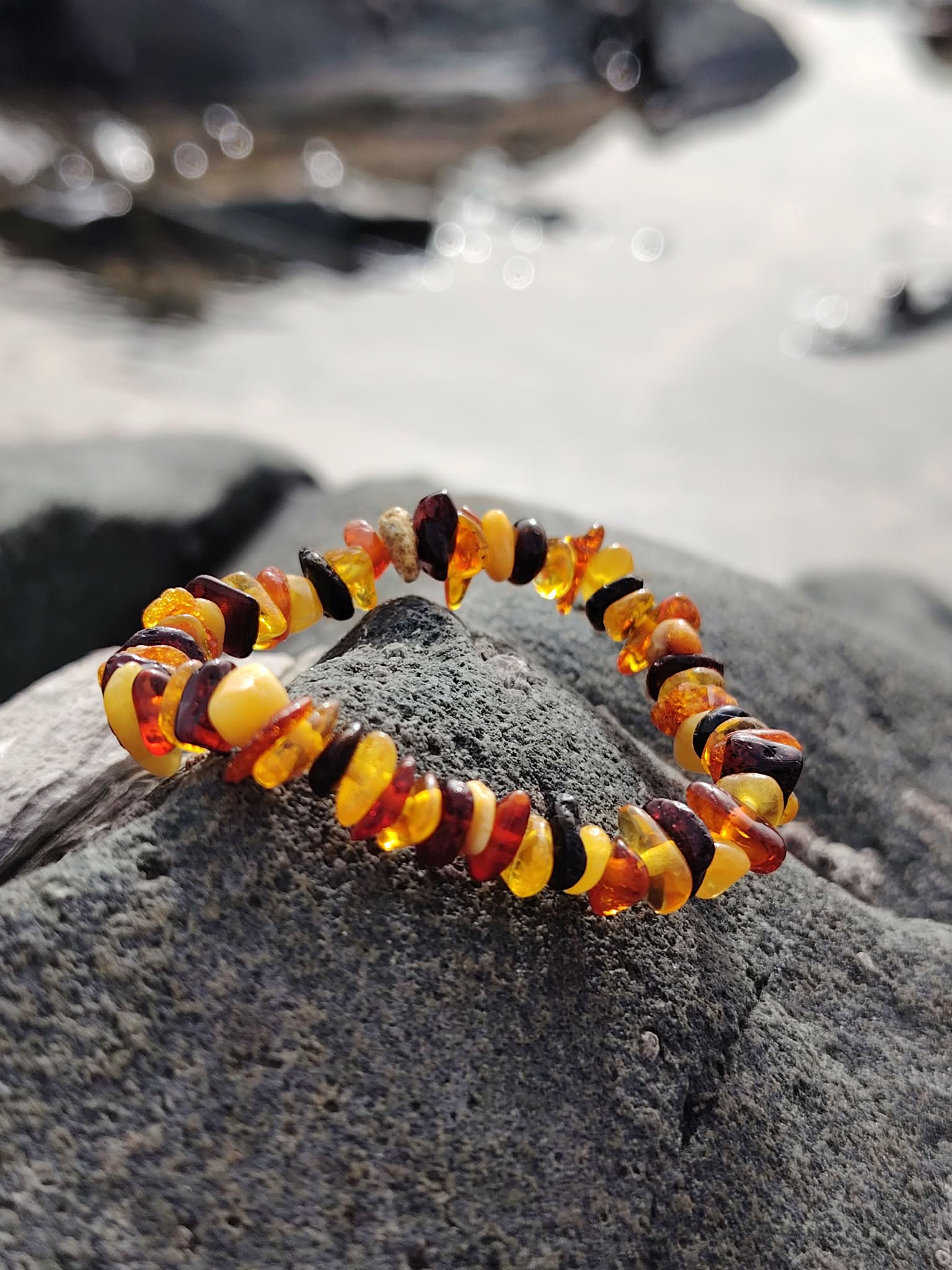 Bracelet enfant en ambre baroque en cercle sur rocher breton, perles miel et cognac, équilibre doux et sensation de réassurance