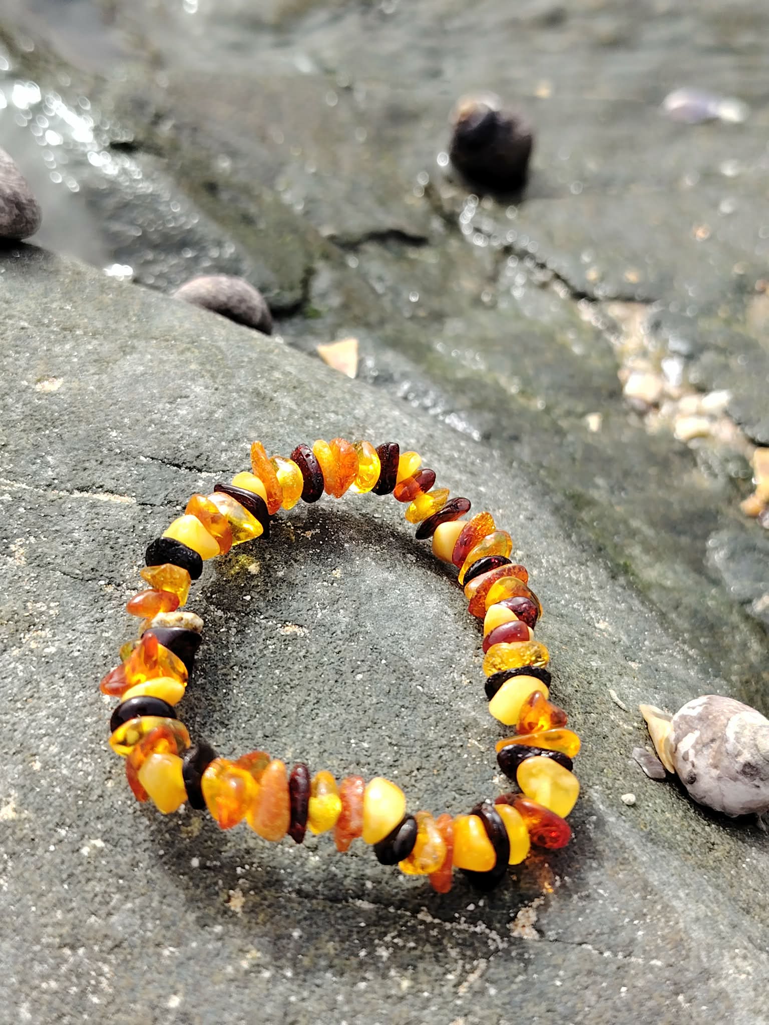 Bracelet enfant ambre baroque formé en cercle sur rocher breton, nuances miel et cognac, apaisement tendre et ambiance lumineuse