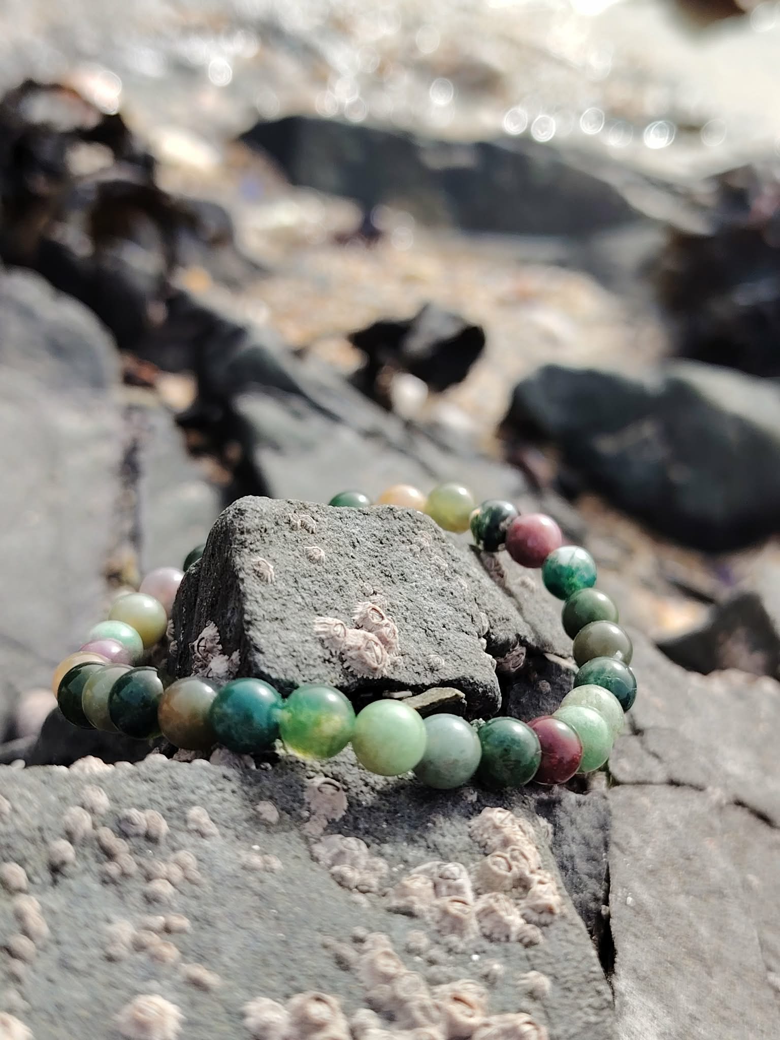 Bracelet Agate Indienne 6 mm en cercle sur rochers bretons, perles vert d’eau et tons terre au milieu des galets, souplesse émotionnelle et constance.