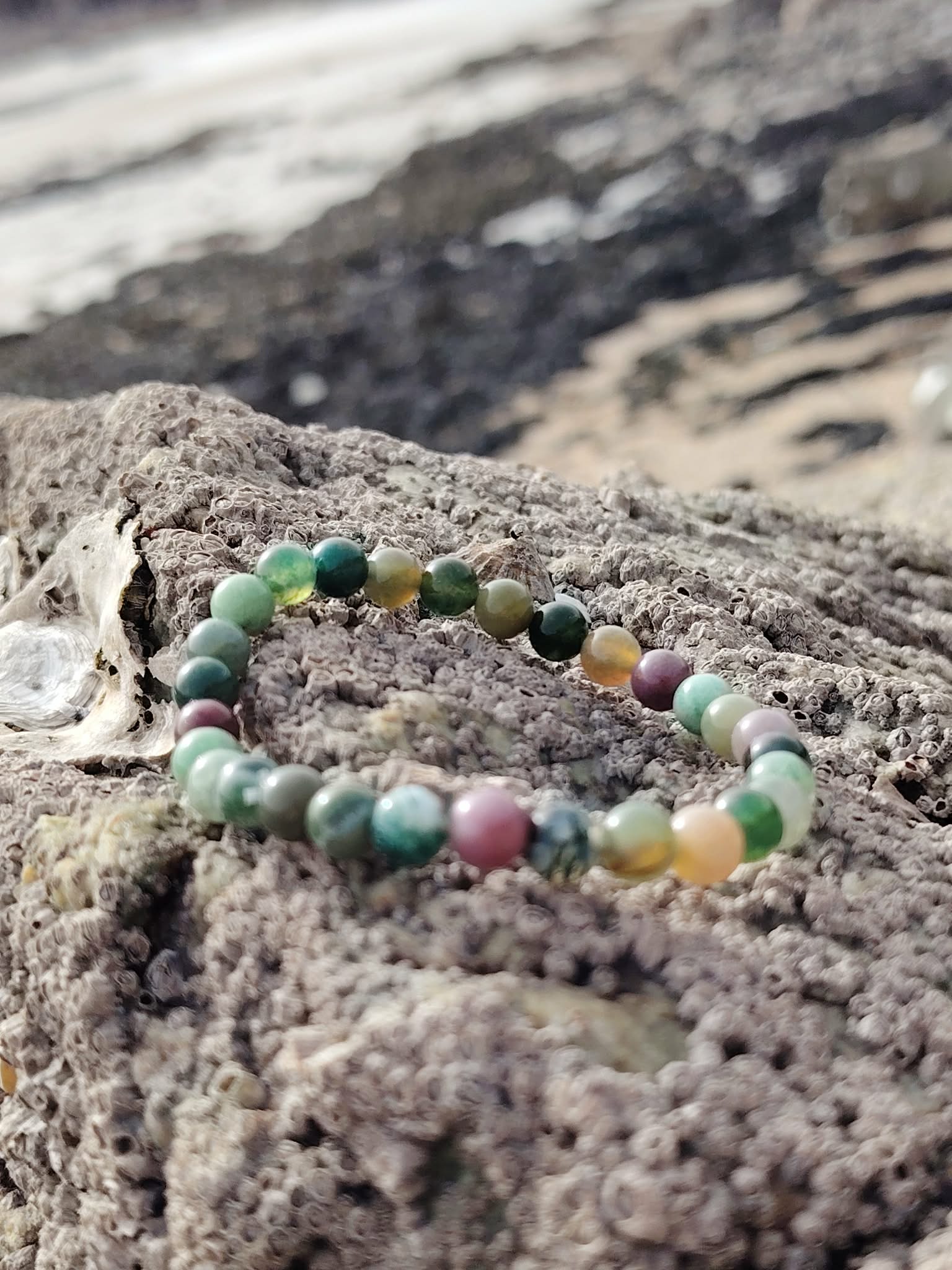 Bracelet Agate Indienne 6 mm sur rocher granitique face à la mer en Bretagne, perles vertes et beige marbrées, sérénité et tenue émotionnelle